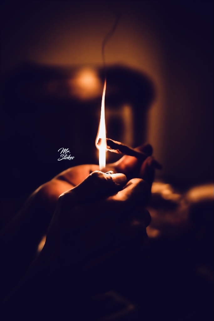 Person lighting a match with a flame, dark background, warm glow, focus on hands and flame.