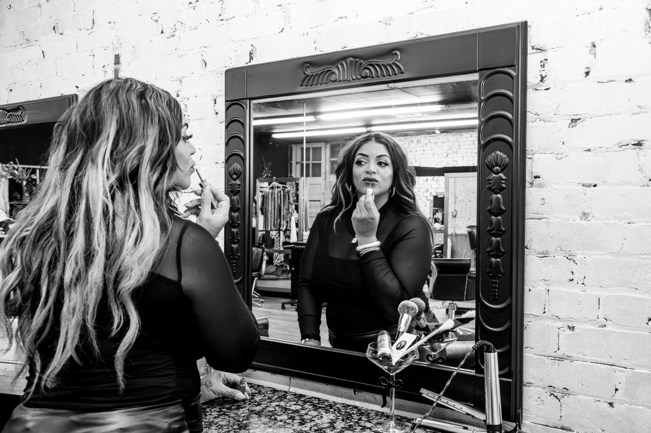 Woman looking at her reflection in a mirror, touching her face, in a room with a brick wall background.