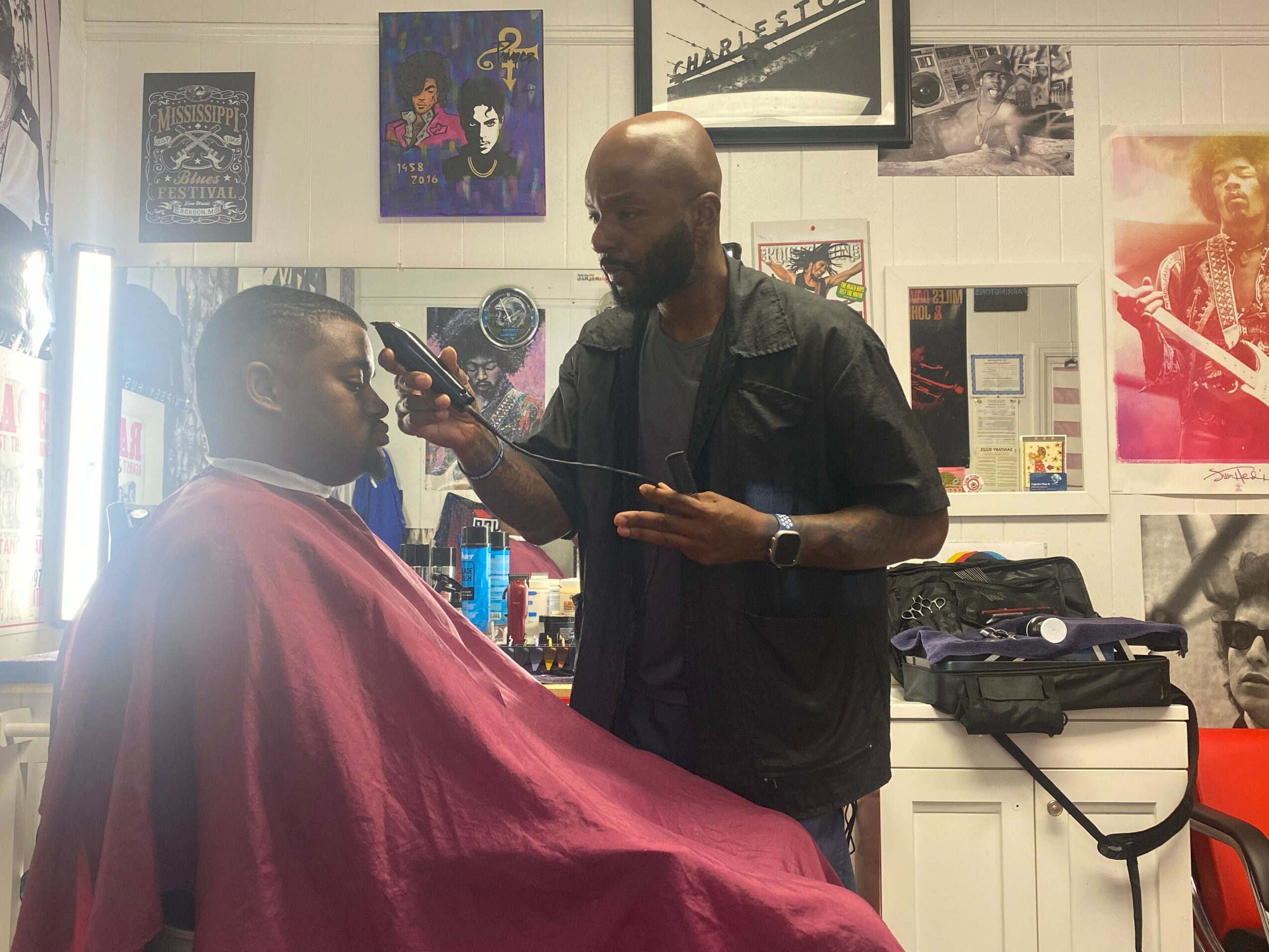 Barber cutting a customer's hair in a barbershop with posters on the wall.