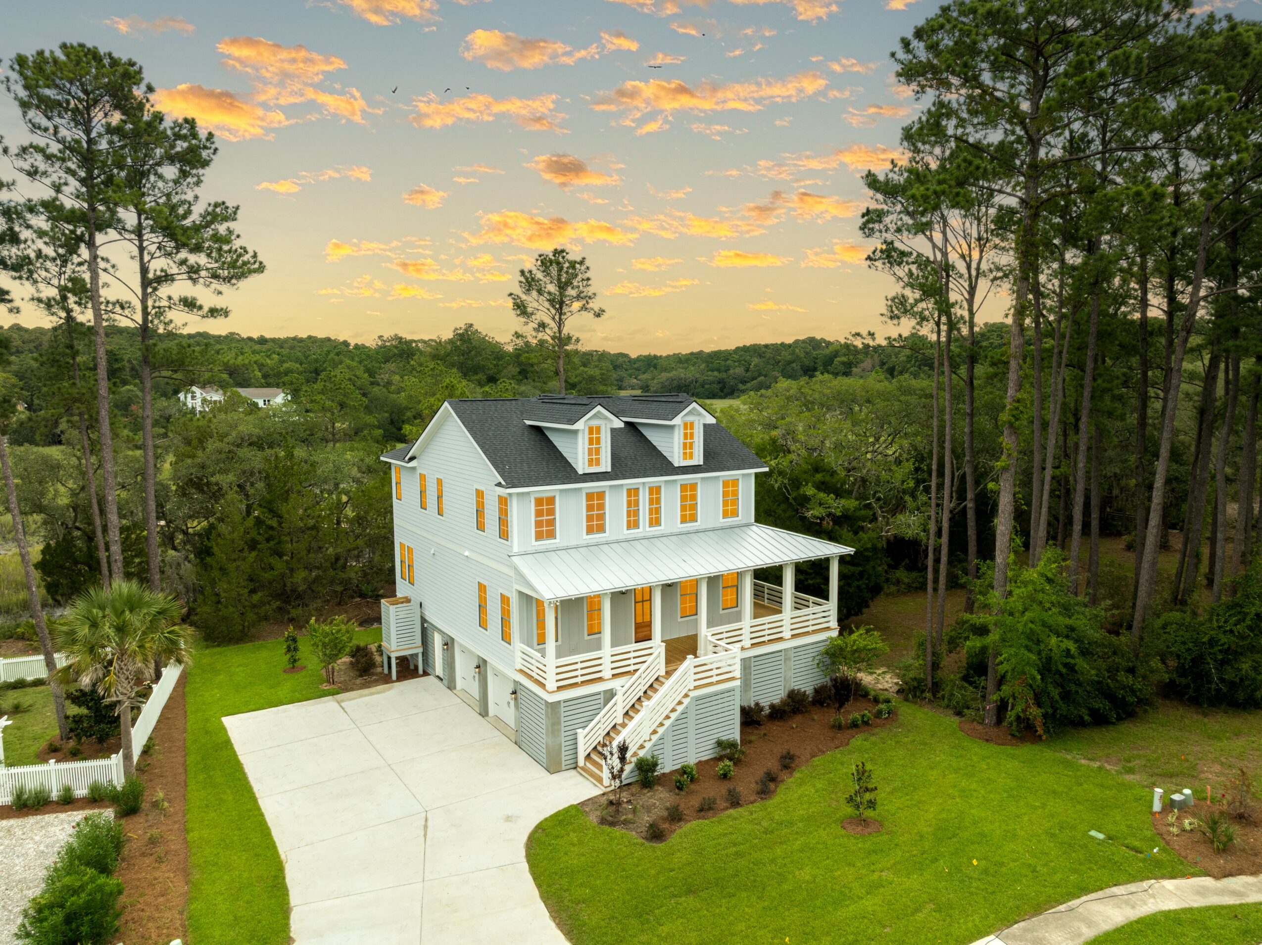 A white house with a porch and stairs, surrounded by trees and a green lawn, under a partly cloudy sky.