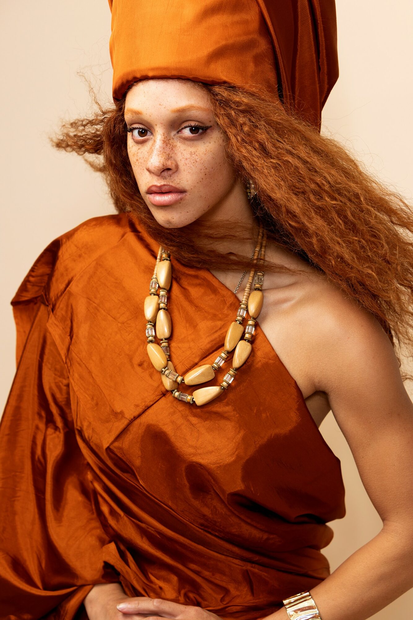 Woman with curly hair wearing an orange headwrap and dress, accessorized with a large beaded necklace.