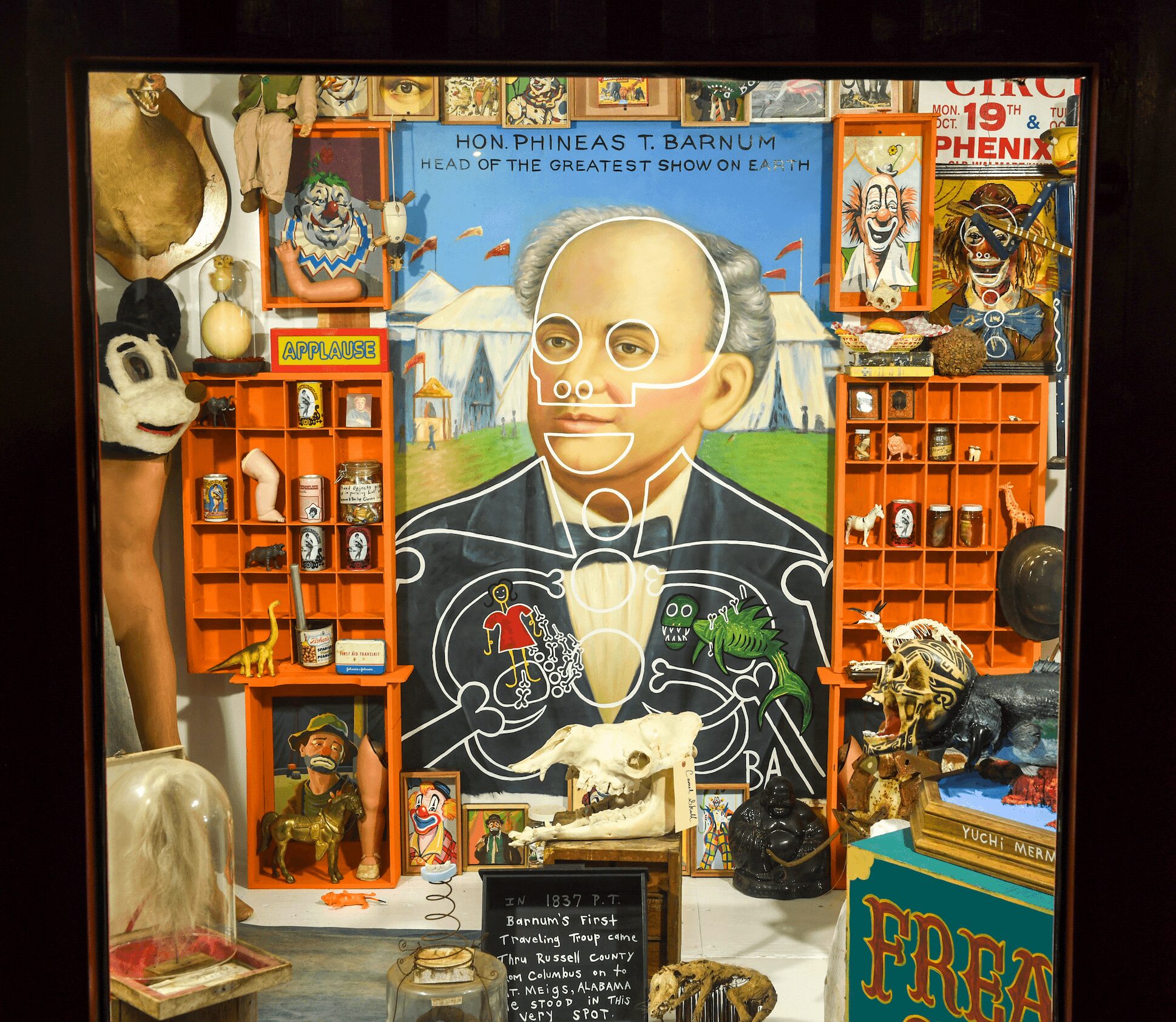 Display with a large portrait of a man, surrounded by various objects, masks, and artwork, including a panda mask and skulls.