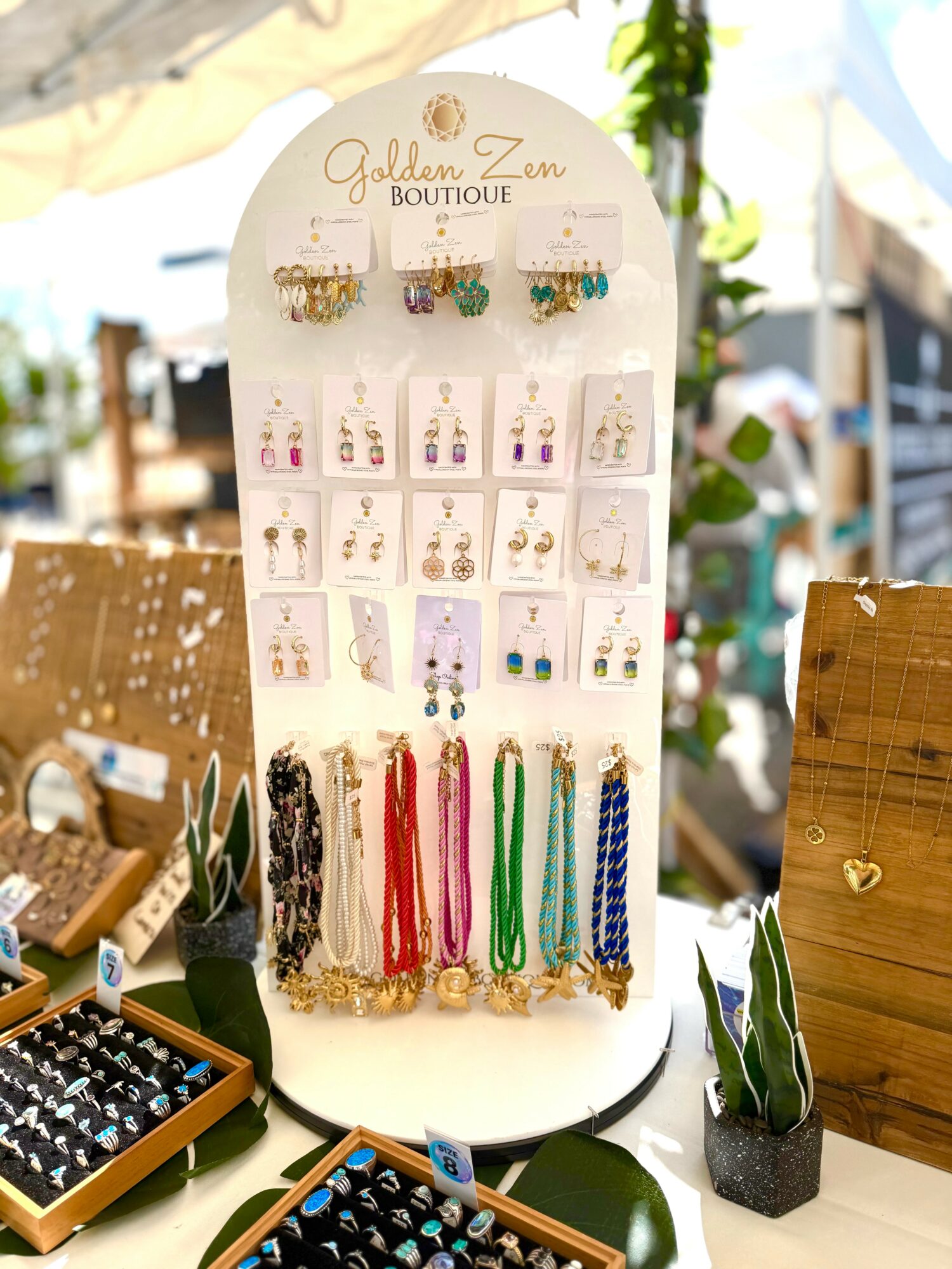 Display stand with earrings and necklaces at an outdoor market, with blurred background and wooden tables.