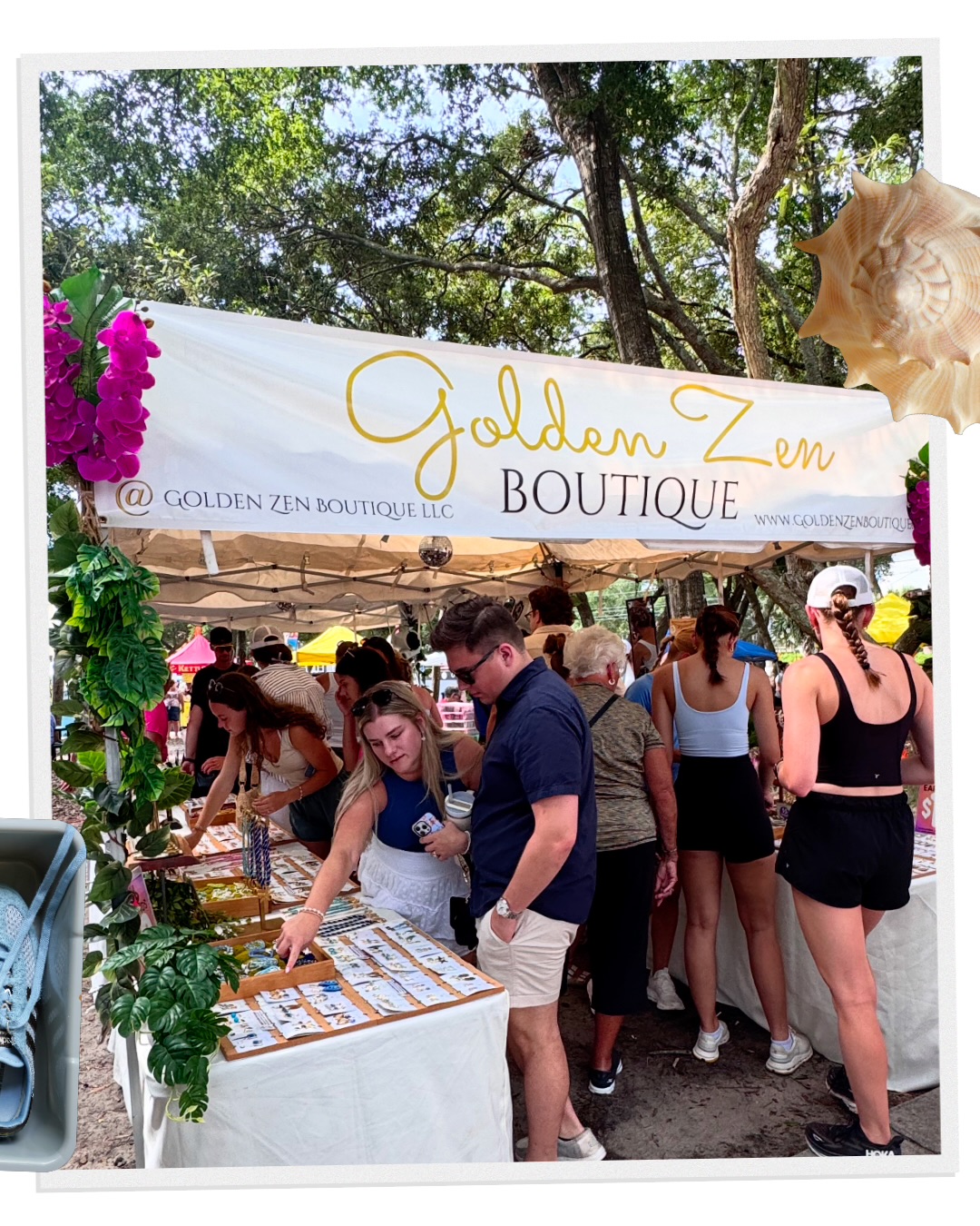 People browsing jewelry at an outdoor boutique under a white canopy with yellow and gold signage, surrounded by trees and flowers.