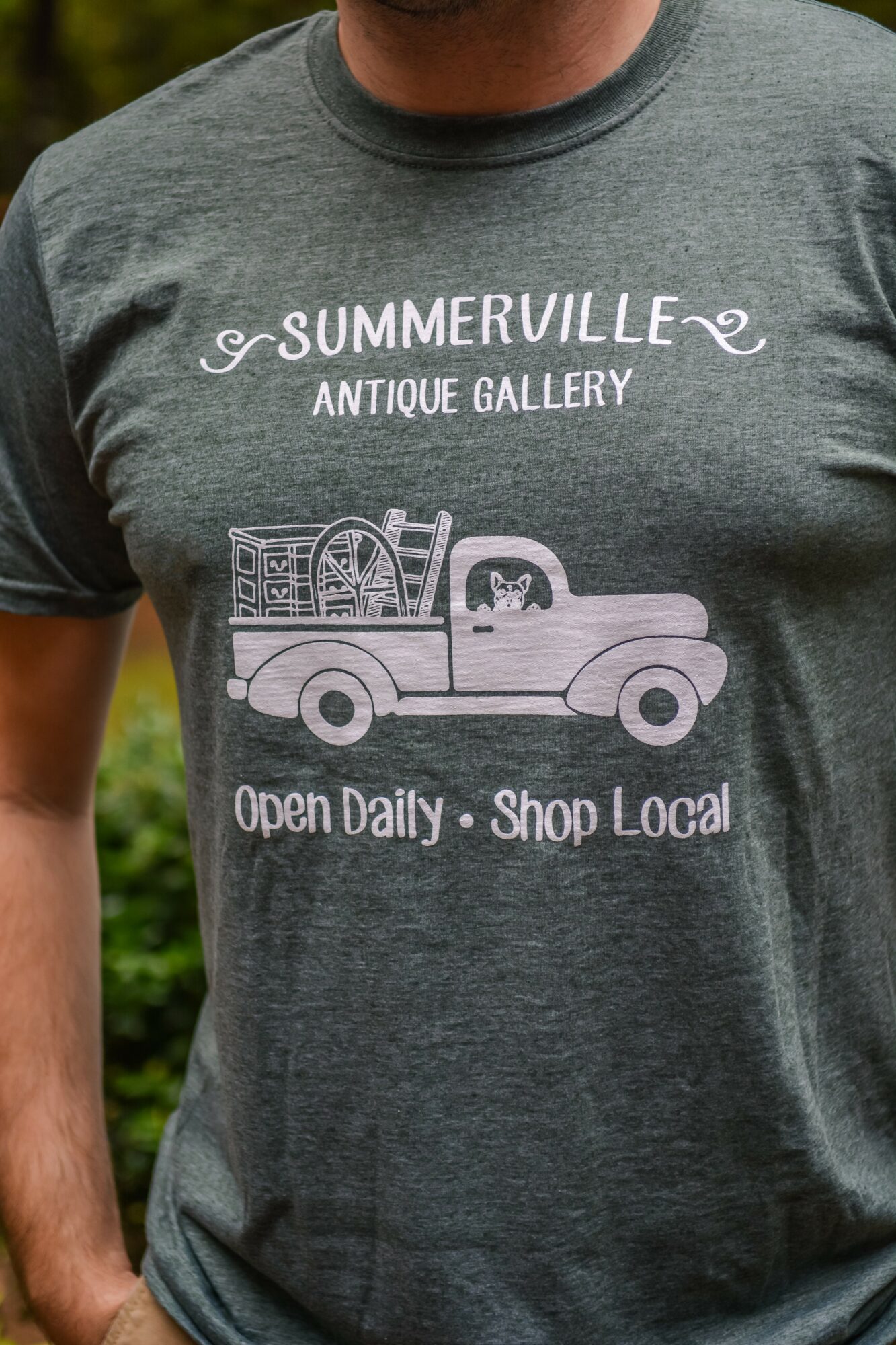 Person wearing a gray T-shirt with a graphic of a truck carrying antique items and text about a local antique gallery.