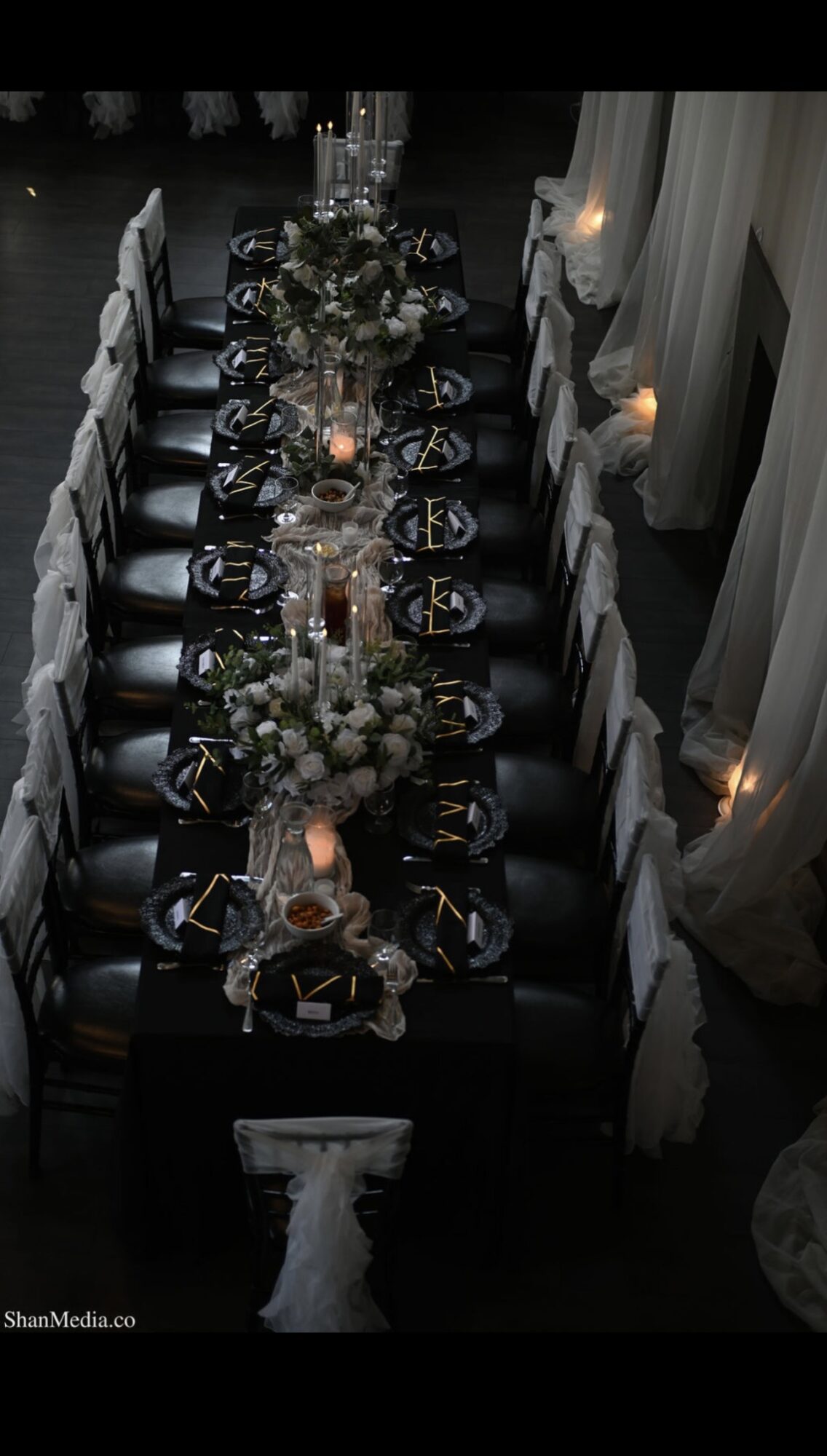 Long dining table set with floral centerpieces, candles, and place settings, viewed from above in a dimly lit room.