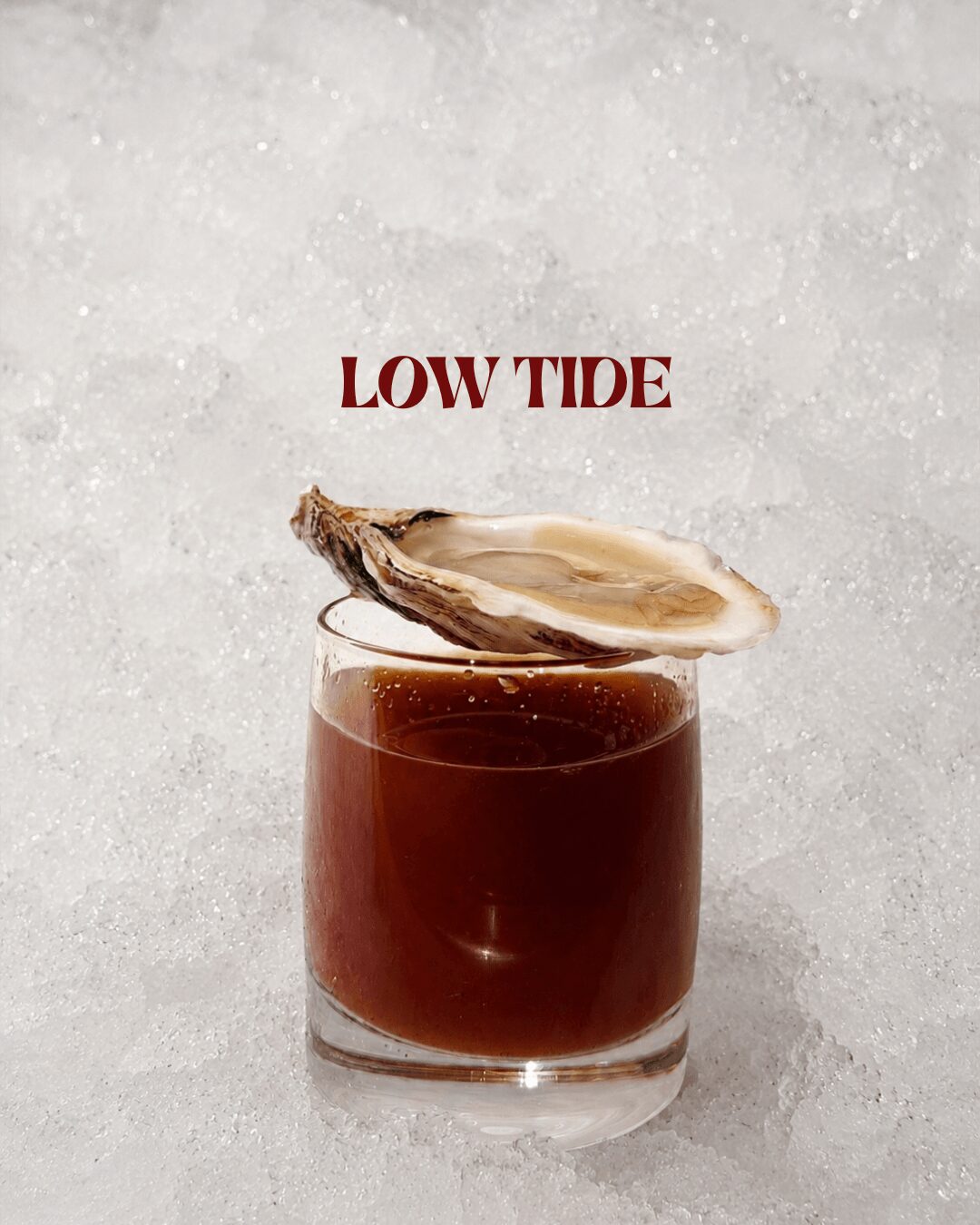 A glass of dark beverage with a shell on top, and the text 'LOW TIDE' above, on a light background.