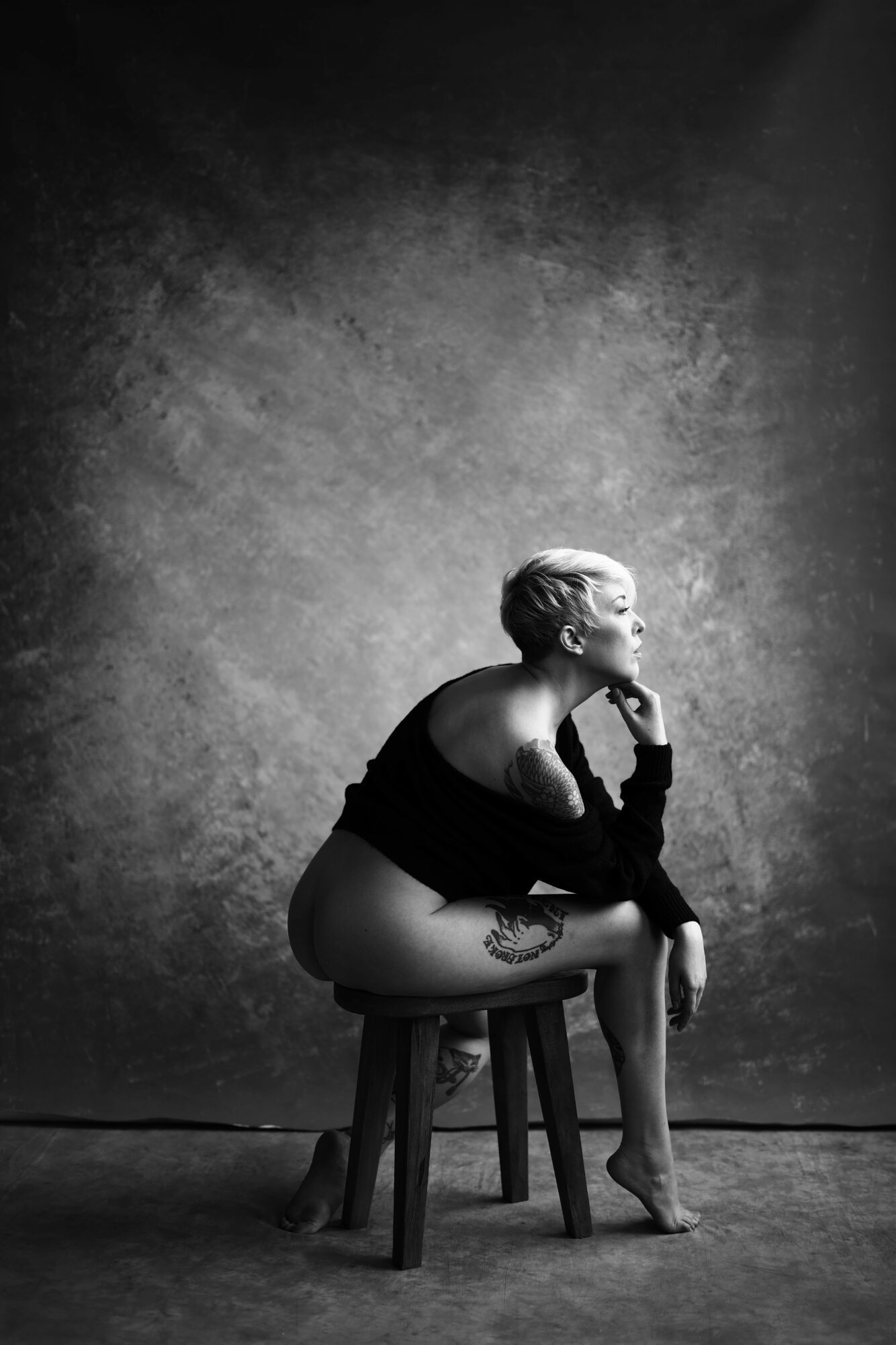 Person sitting on a chair, leaning forward, with a textured wall background, in black and white.