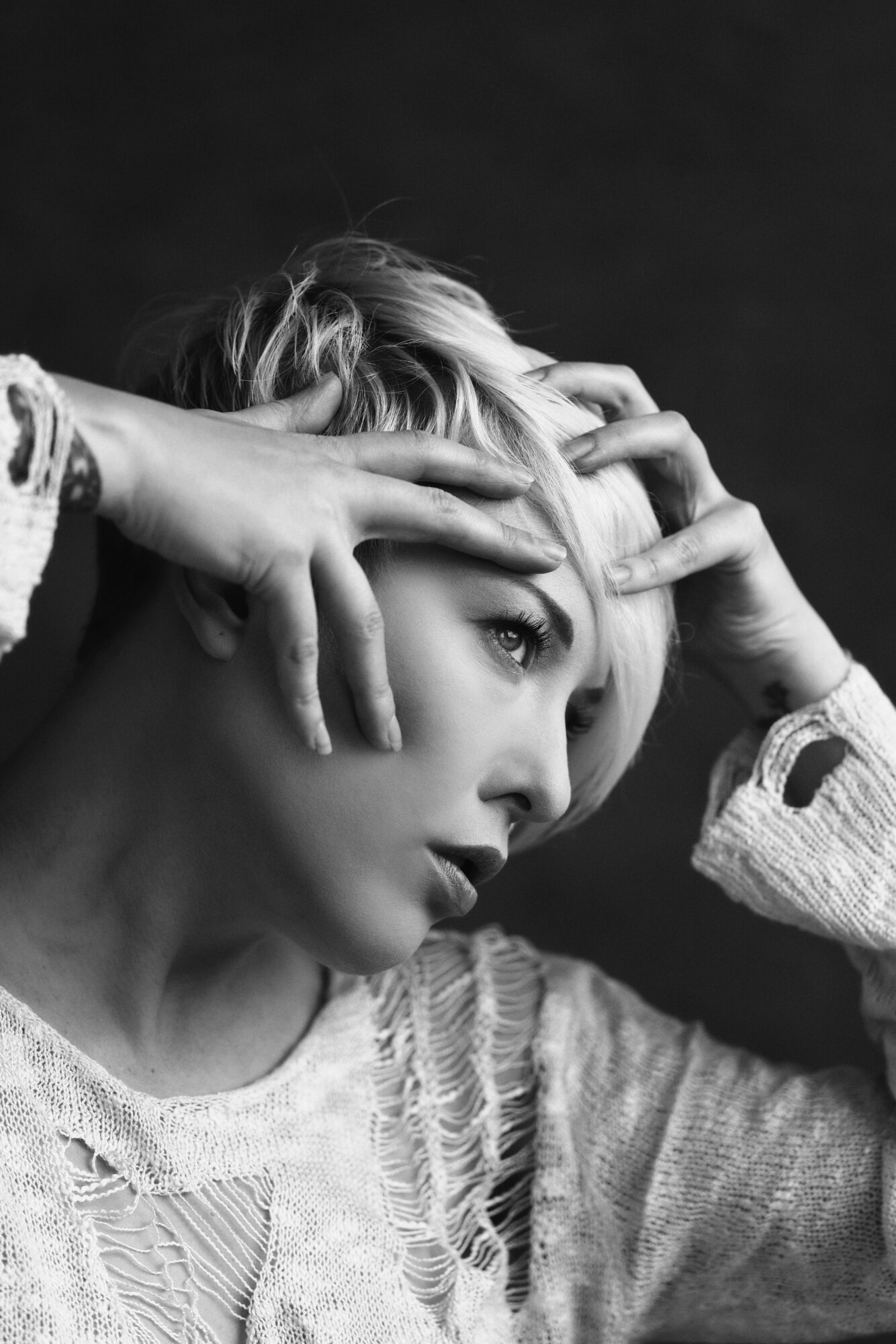 Black and white portrait of a woman with short hair, hands on her face, looking to the side.