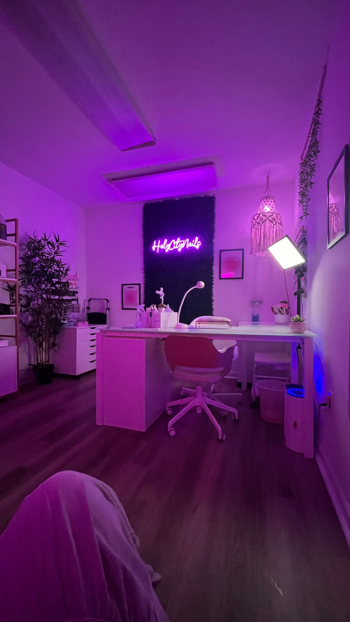 Office with purple lighting, desk, chair, plants, and decorative chandelier, viewed from the floor. Word 'Hello' on wall. Word count: 20