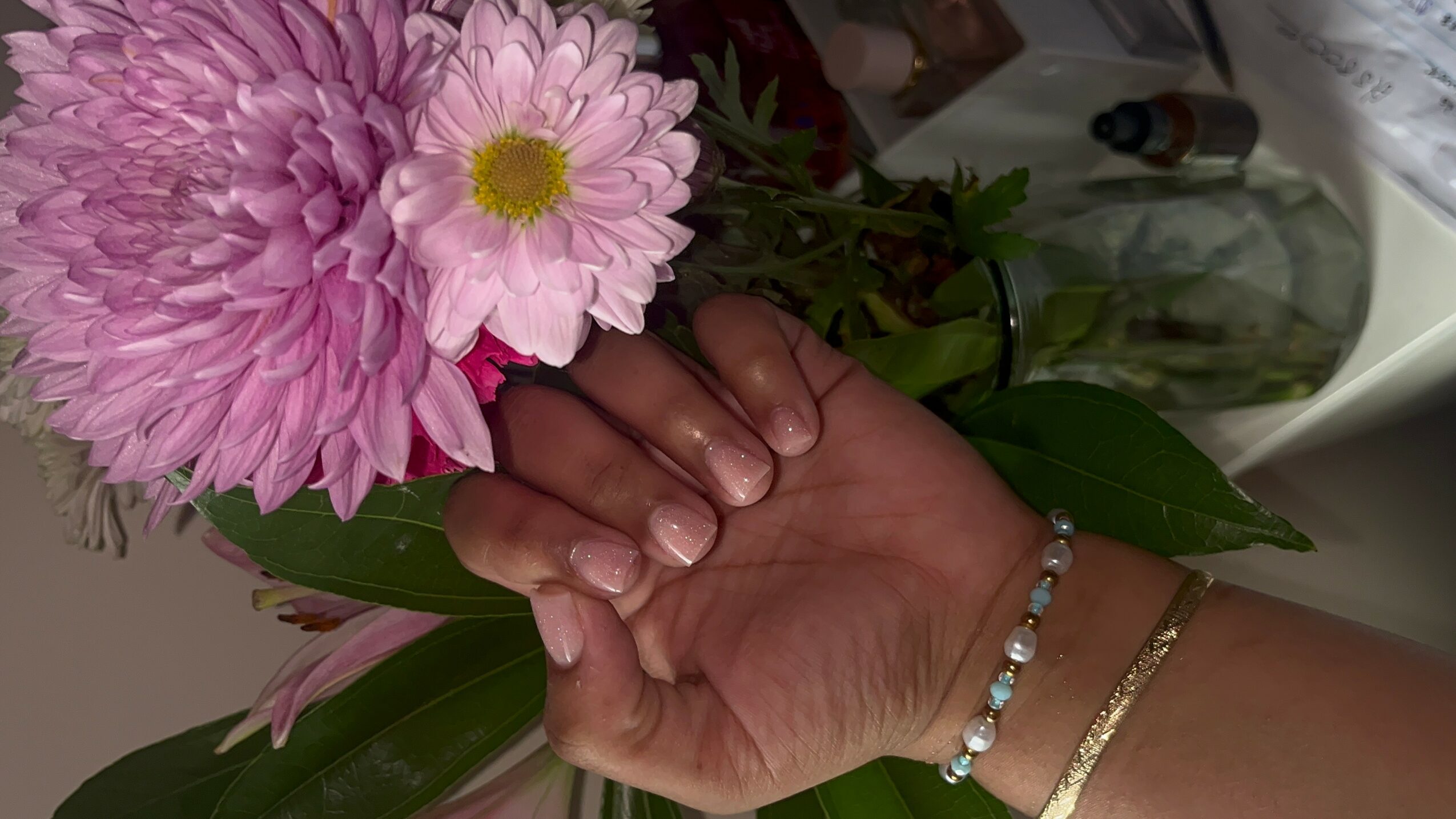 Person's hand holding pink and purple flowers, with a bracelet and a gold bracelet visible.