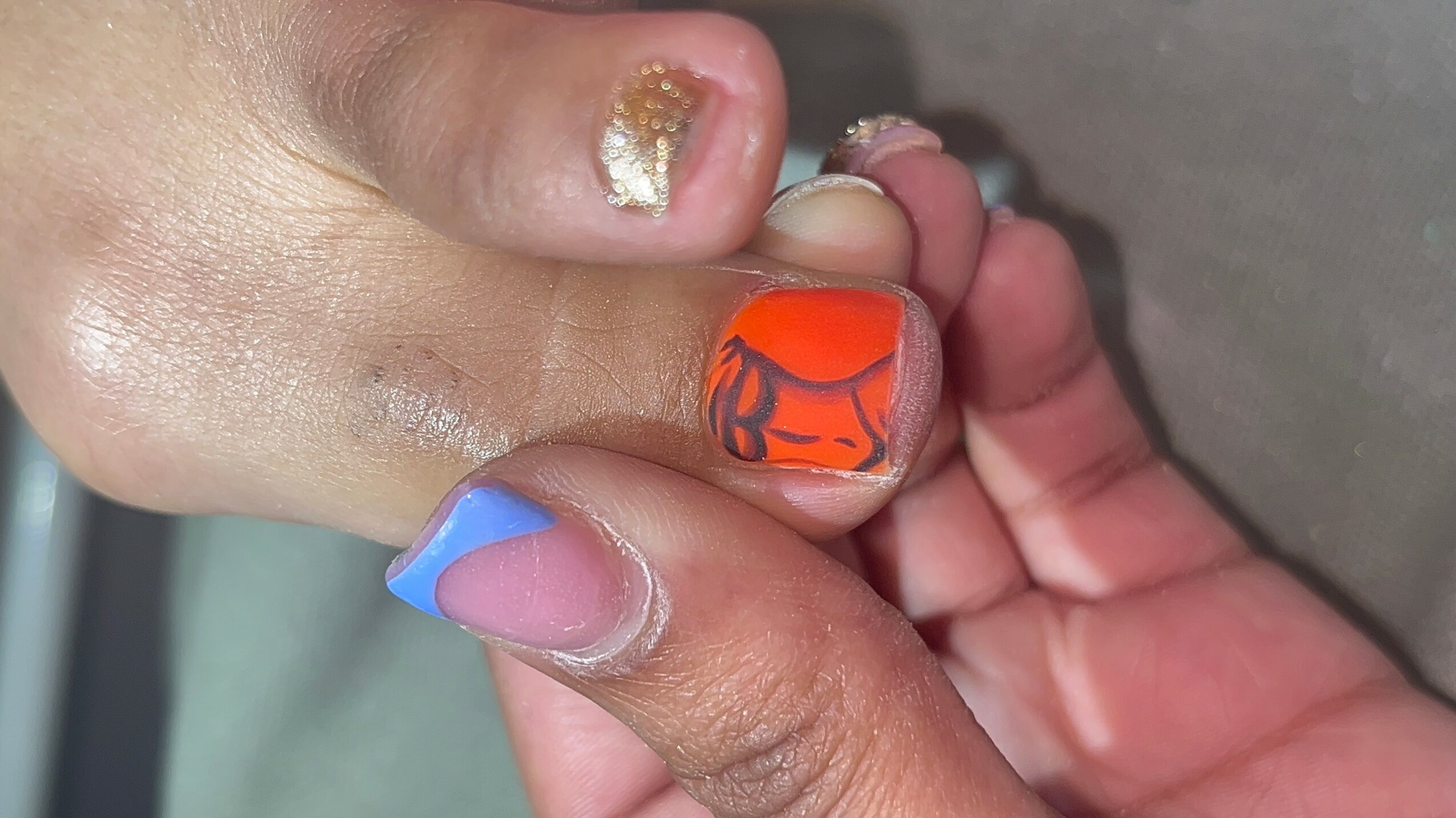 Close-up of a person's hand with colorful nail art, including orange, blue, and gold designs.