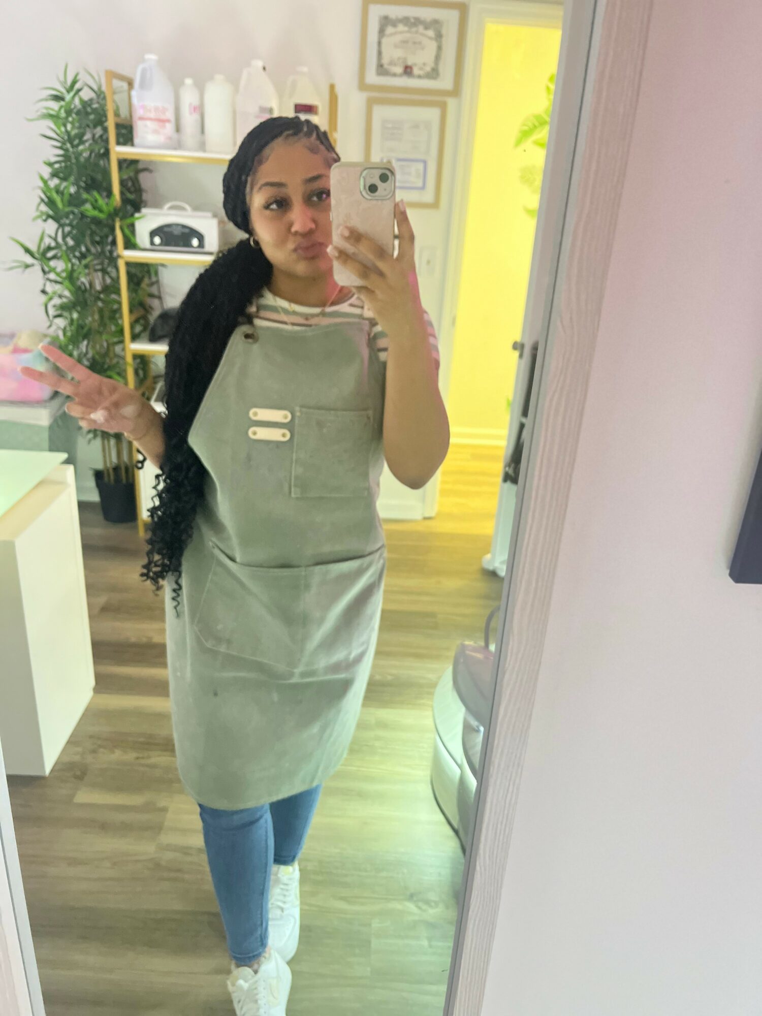 Young woman with long dark hair taking a mirror selfie in a room with light-colored walls and wooden flooring.