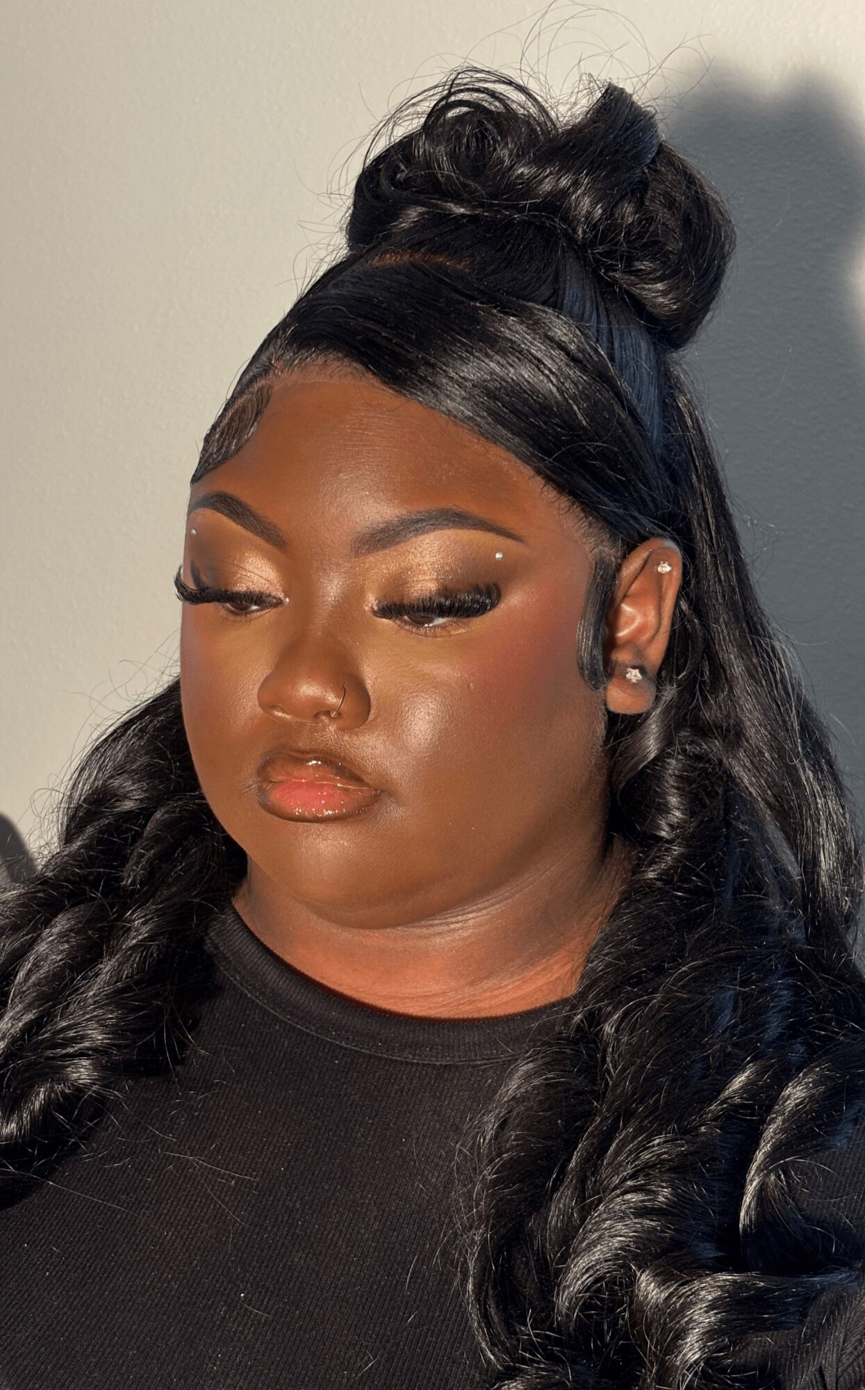 Close-up of a woman with styled hair and makeup, wearing a black top, looking downward.