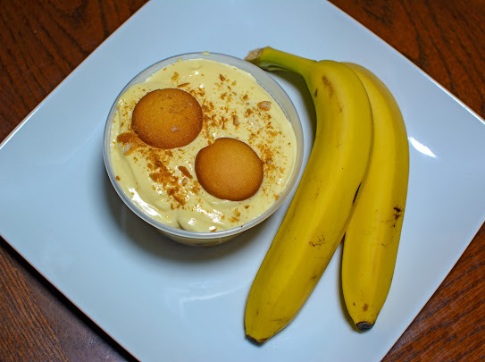 Cup of dessert with two round cookies, bananas on a white plate, on a wooden table.
