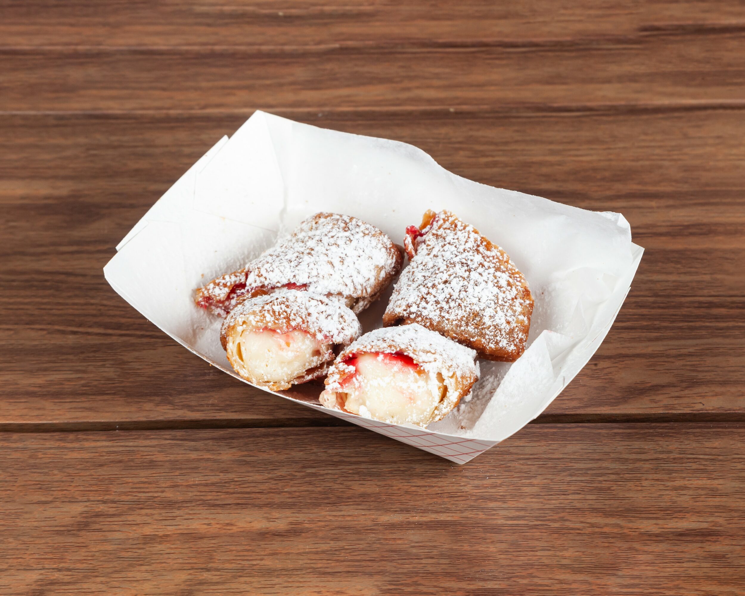 Three cannoli pastries dusted with powdered sugar in a paper tray on a wooden surface.