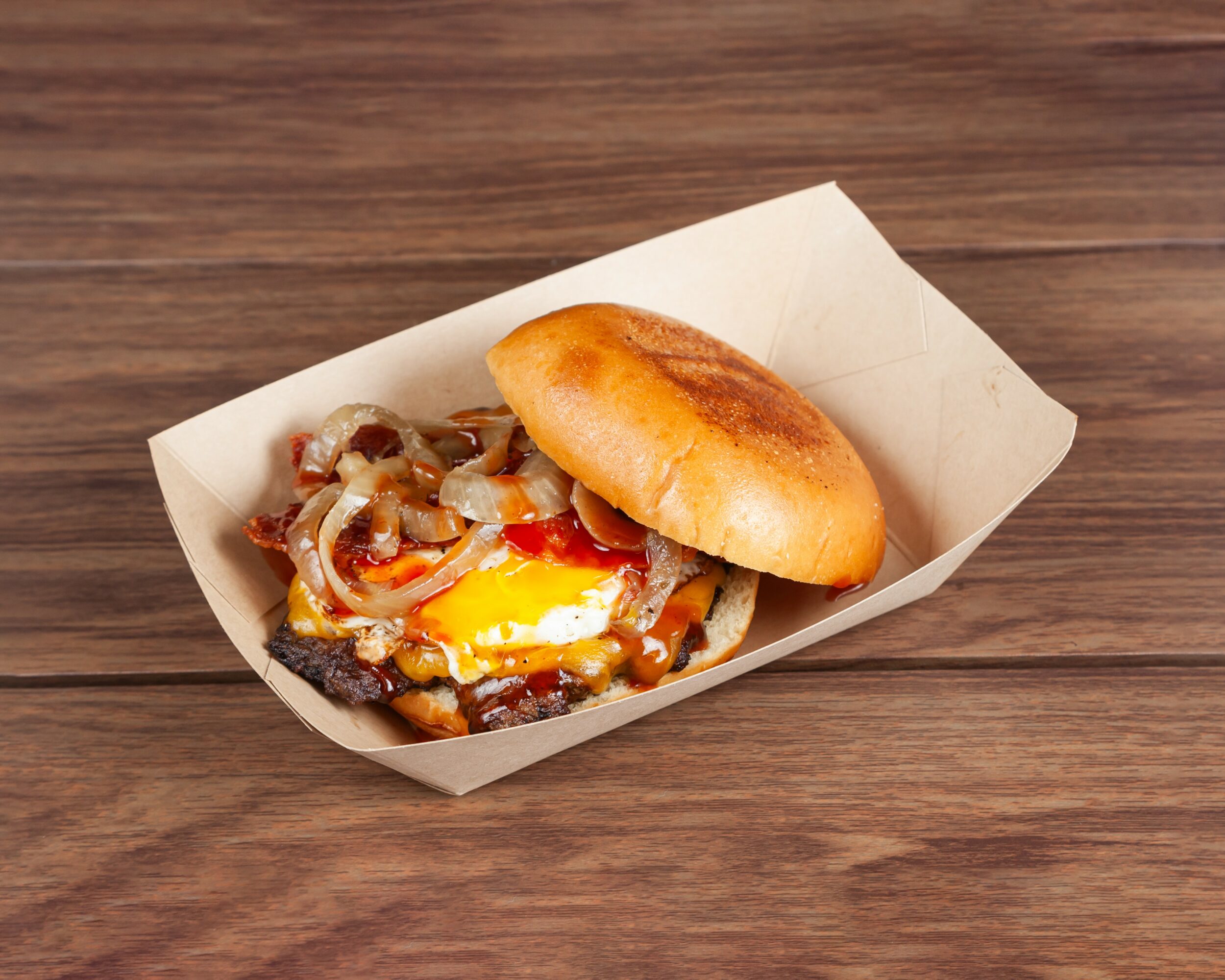Burger with fried egg, vegetables, and bun in a paper tray on wooden surface