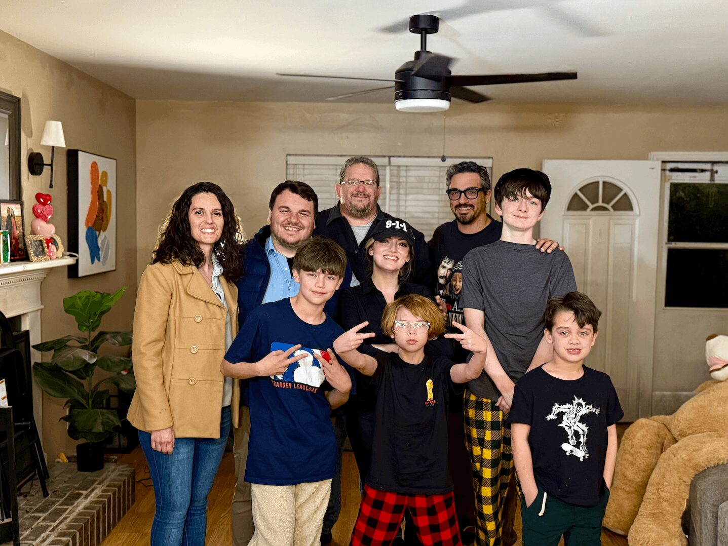 Group of nine people, including children and adults, standing in a living room, smiling at the camera.