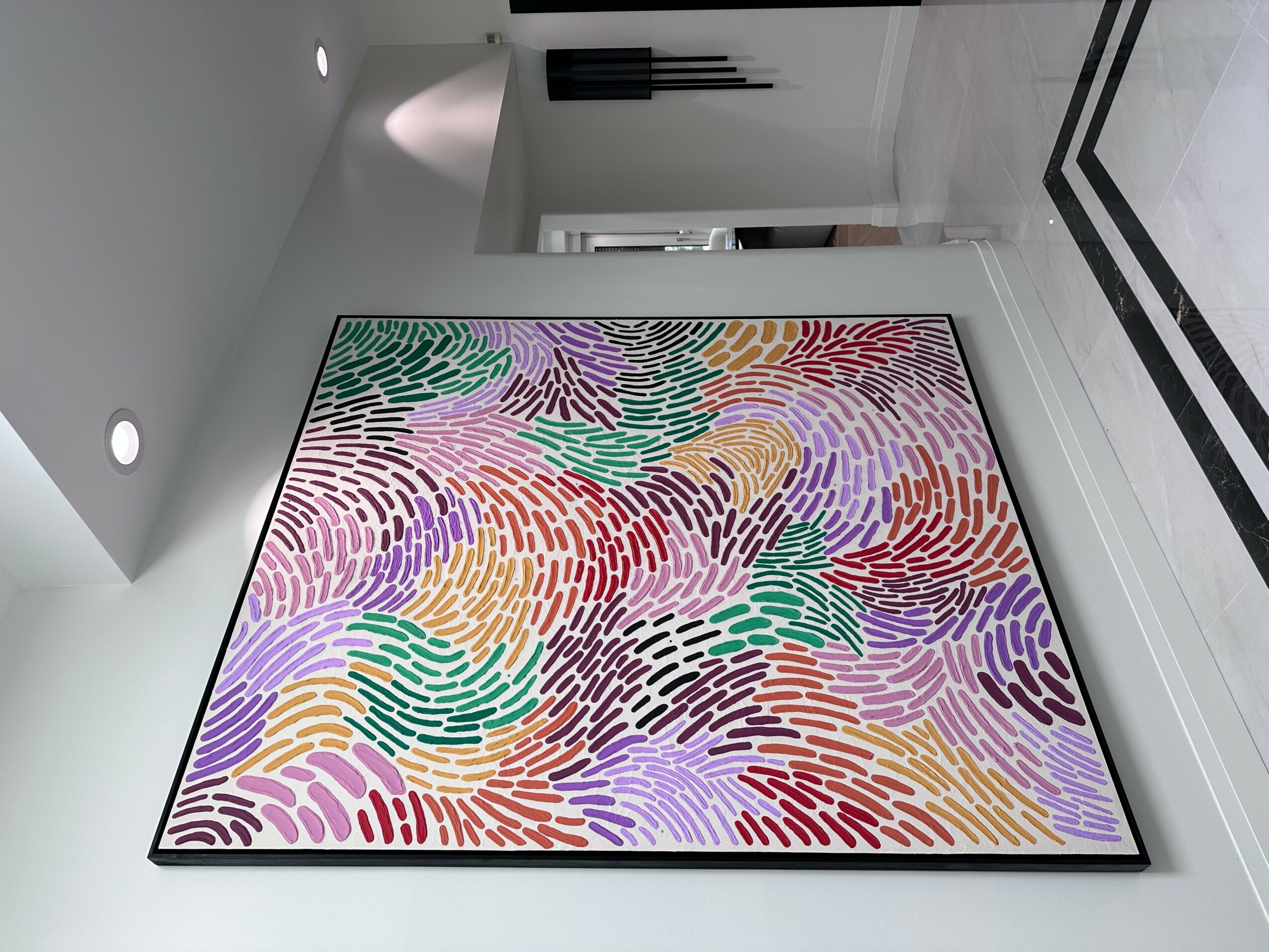 Colorful abstract painting with wavy lines in various colors on a white wall.