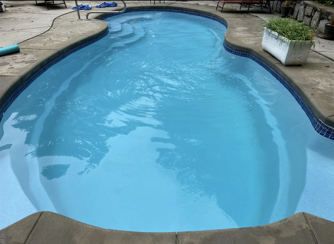 Swimming pool with clear blue water, surrounded by concrete and potted plants.