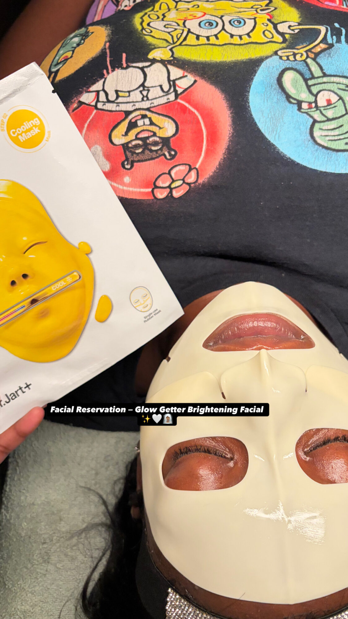 Person holding a yellow smiley face mask, with a mask of a face with closed eyes and lips, and a shirt with SpongeBob characters.