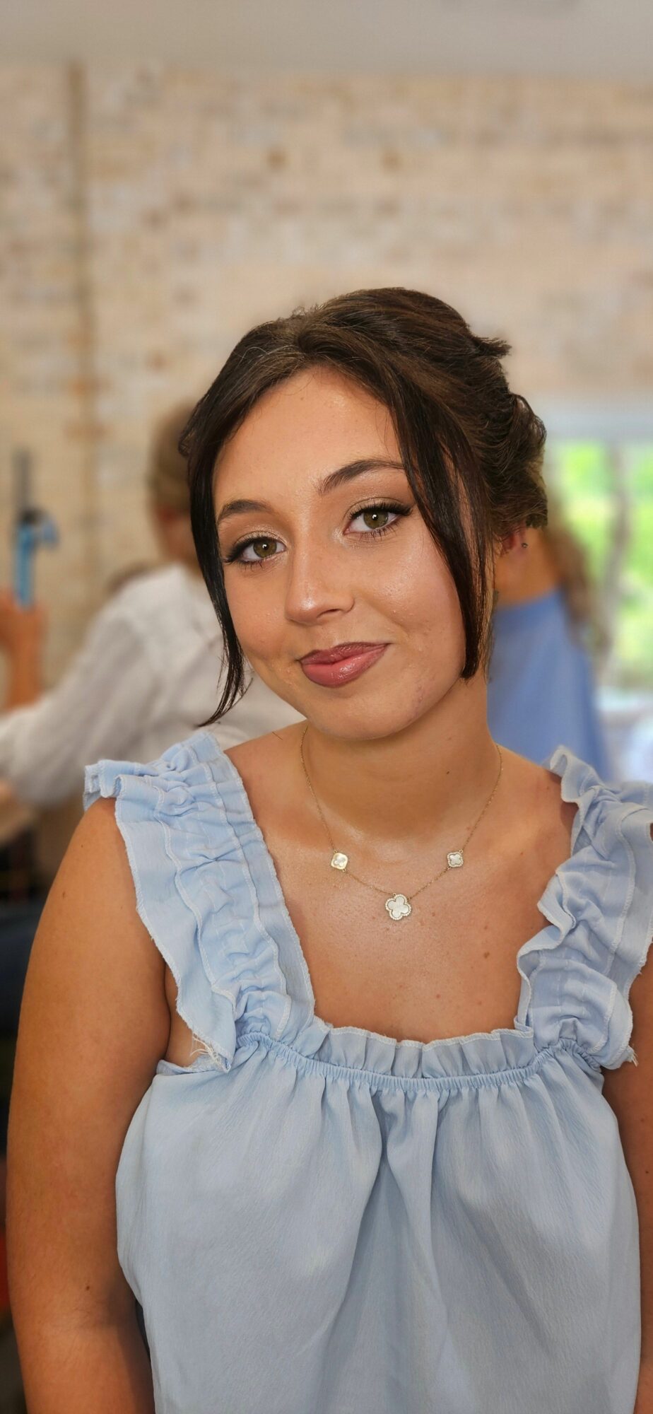 Young woman with dark hair in a light blue dress, smiling, outdoors with a blurred background.