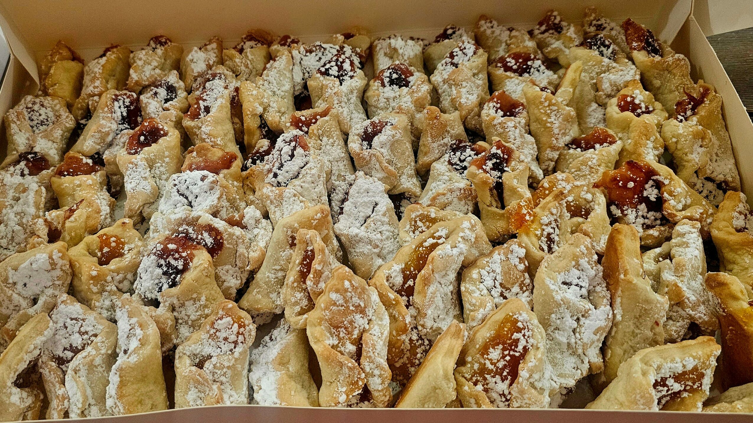 A box filled with small pastries dusted with powdered sugar, some with fruit filling or toppings.