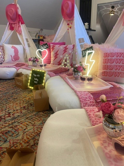 Decorative setup with pink and white elements, tents, pillows, and neon signs on a patterned carpet.