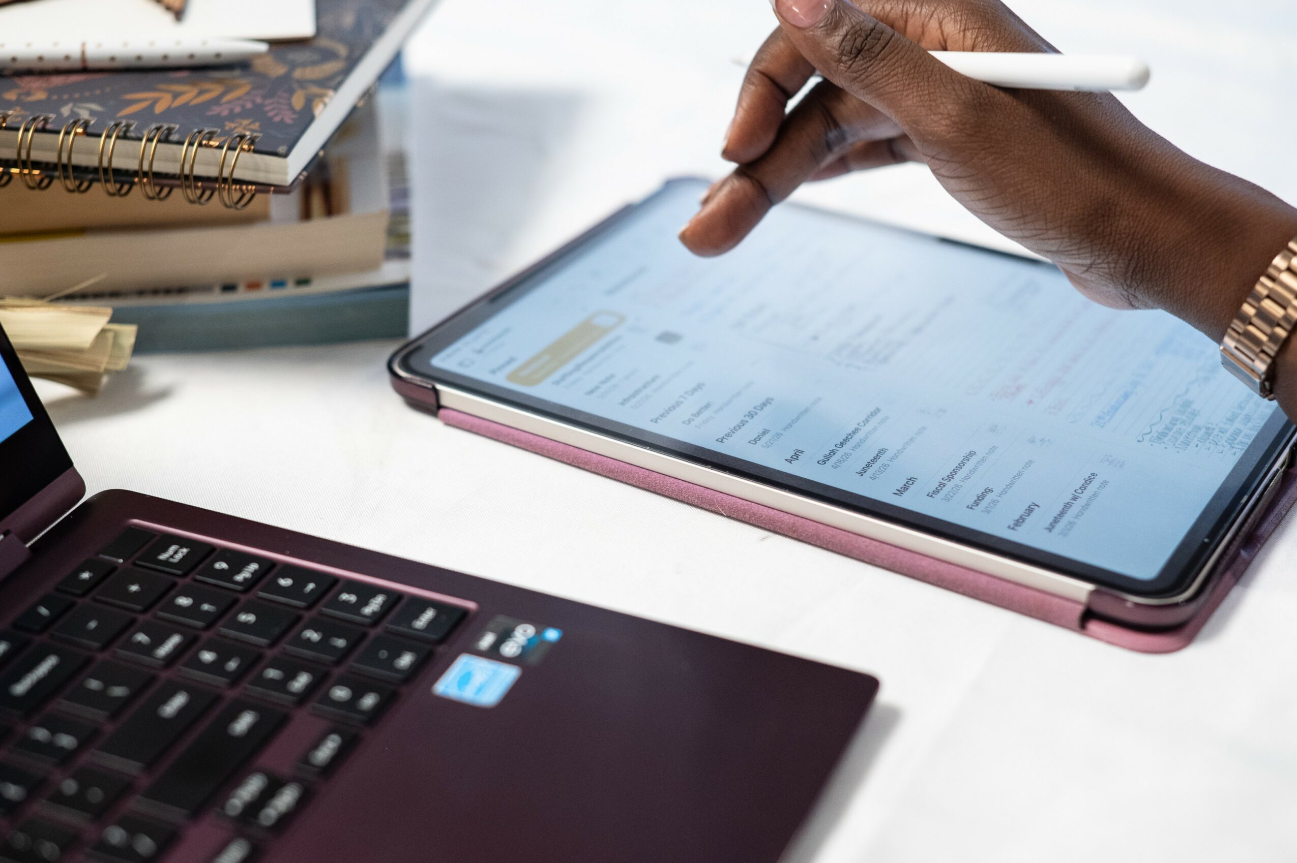 Person using a stylus on a tablet with a keyboard nearby on a white desk.