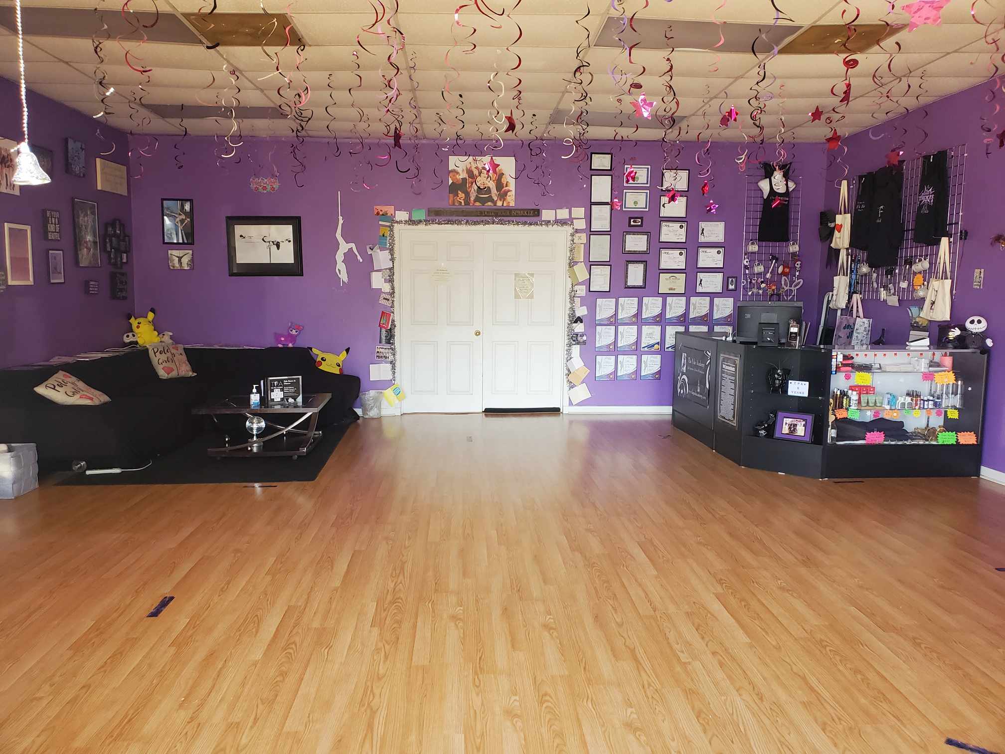 Room with purple walls, black sofa, display shelves, and decorations hanging from the ceiling, with a wooden floor.