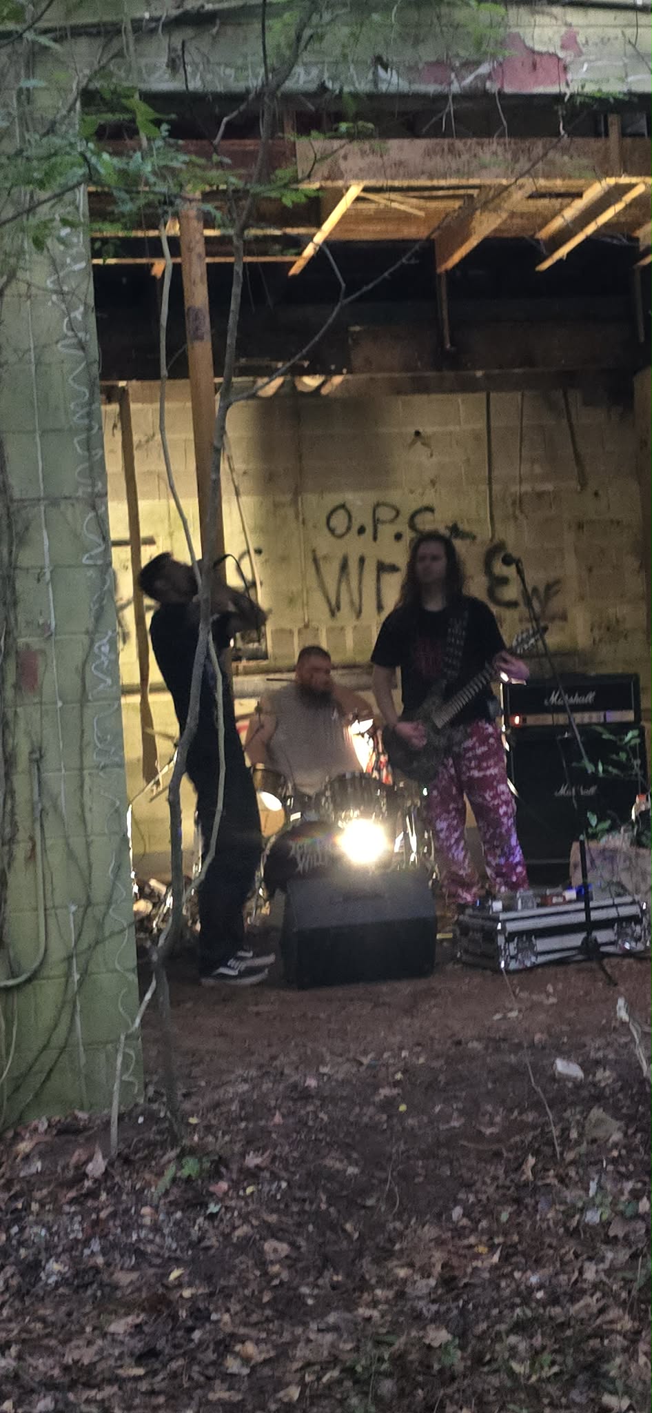 Two people performing on a stage outdoors, with musical equipment and a graffiti-covered wall in the background.