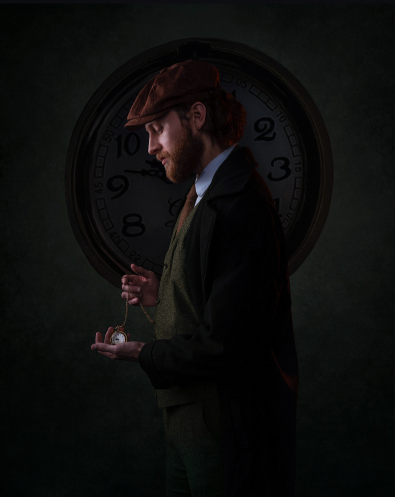 Man in suit holding a glass, standing in front of a large clock, with dark background.