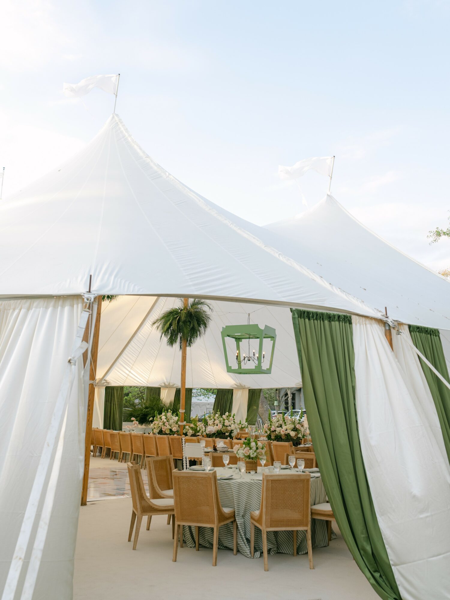 Large white tent with green curtains, decorated for an outdoor event with tables and chairs, under a clear sky.