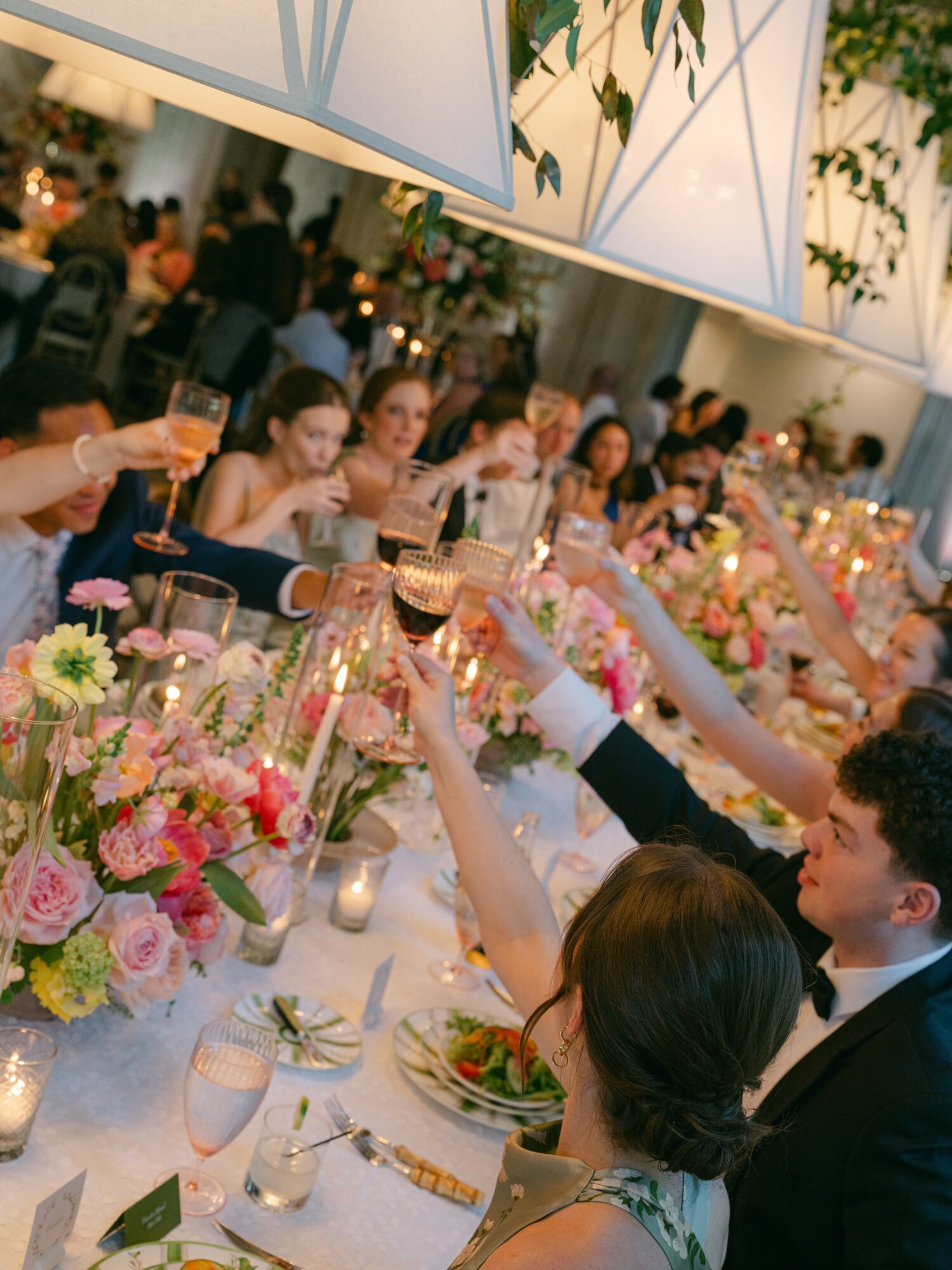 People raising glasses at a decorated banquet table with flowers and candles, celebrating in a festive setting.