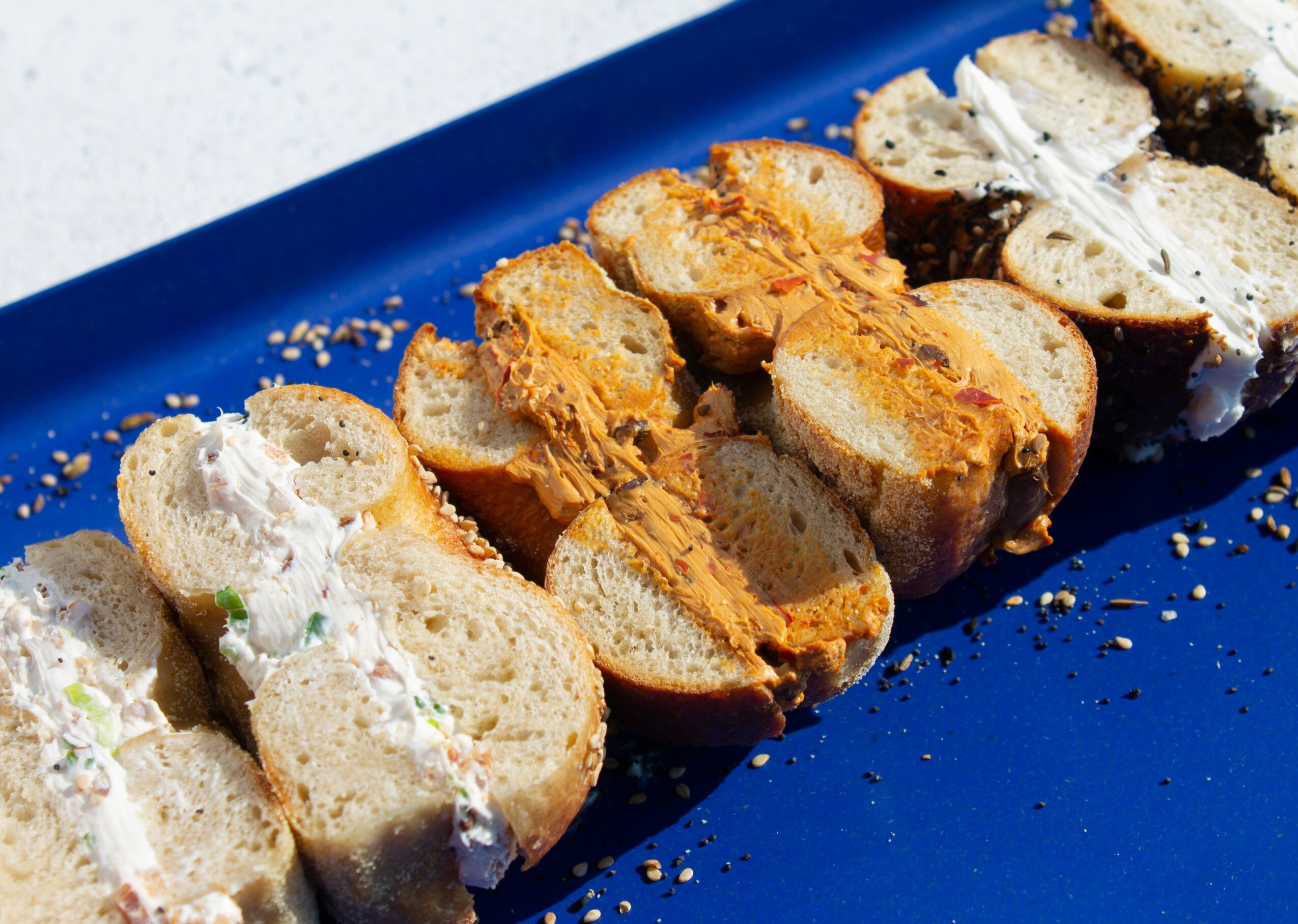 Assorted bread slices with various toppings on a blue tray, some with spreads and others with toppings, sprinkled with crumbs.