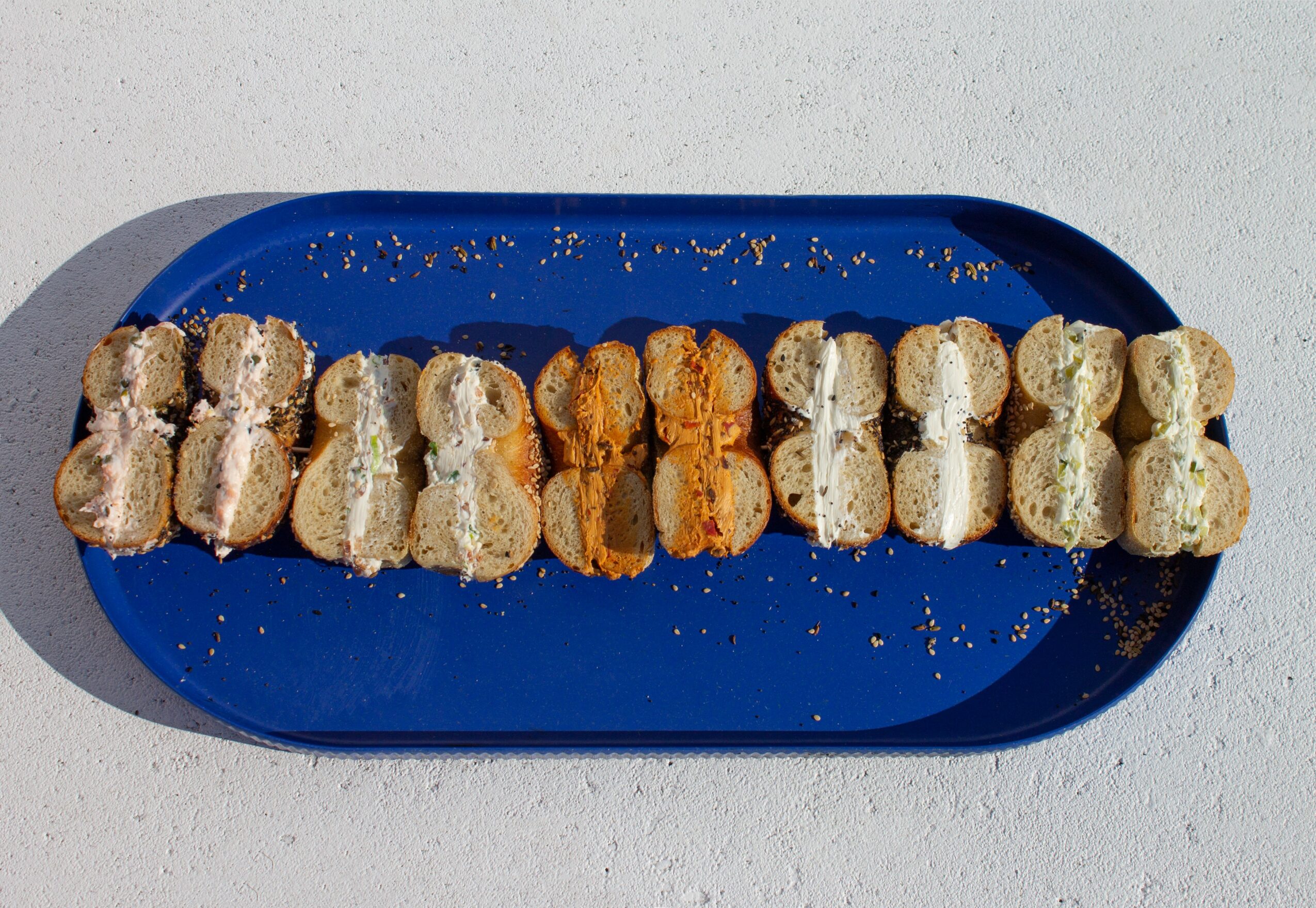 A blue tray with sushi rolls arranged in a line on a light surface, some with sesame seeds and orange fish roe.