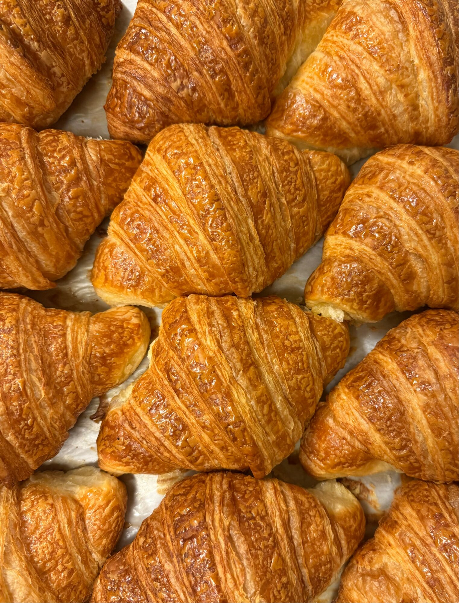 Close-up of multiple golden-brown croissants arranged together, showing flaky layers and crispy texture.