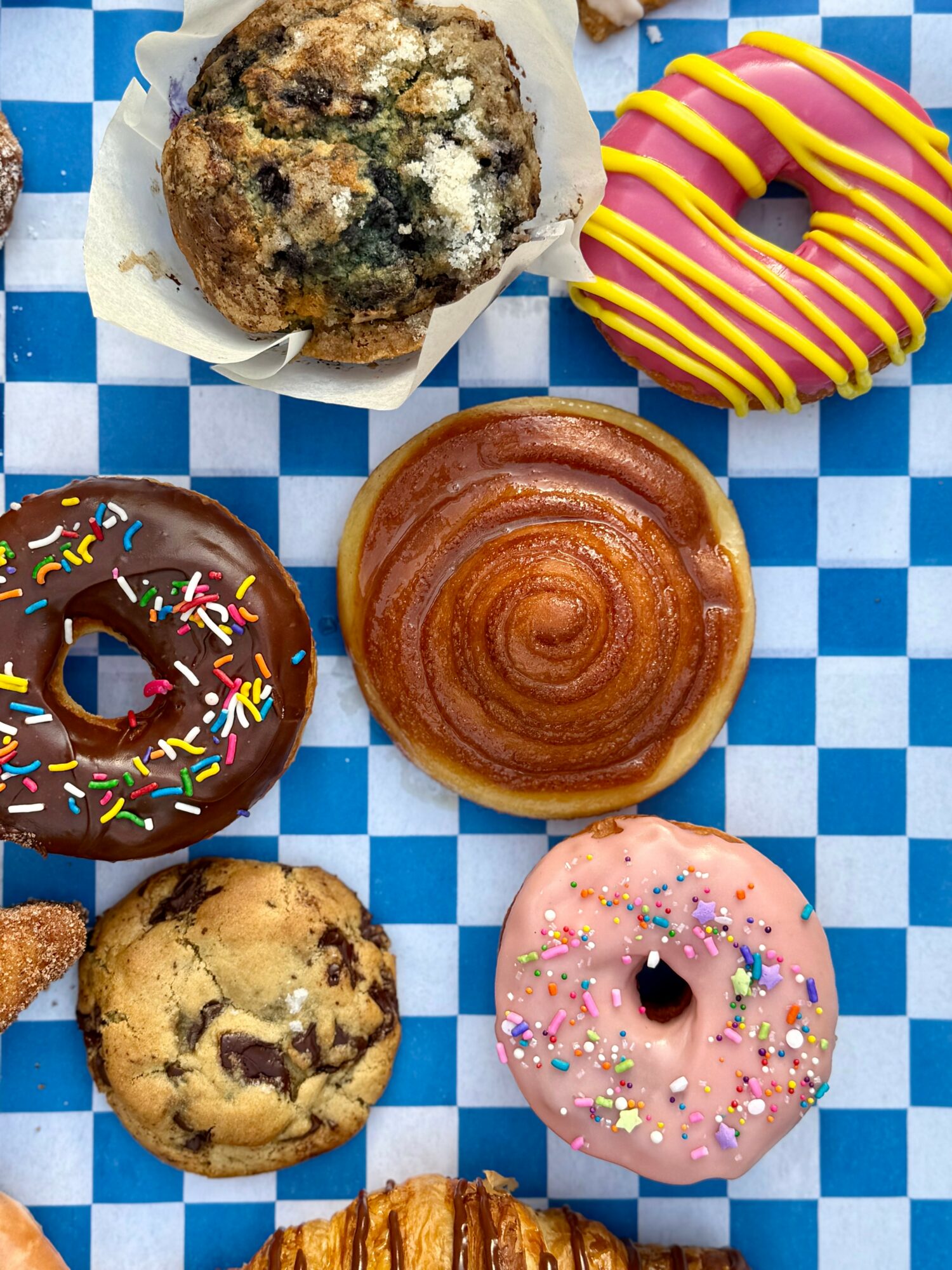 Six assorted donuts on a blue and white checkered surface, including chocolate, glazed, and sprinkled varieties.