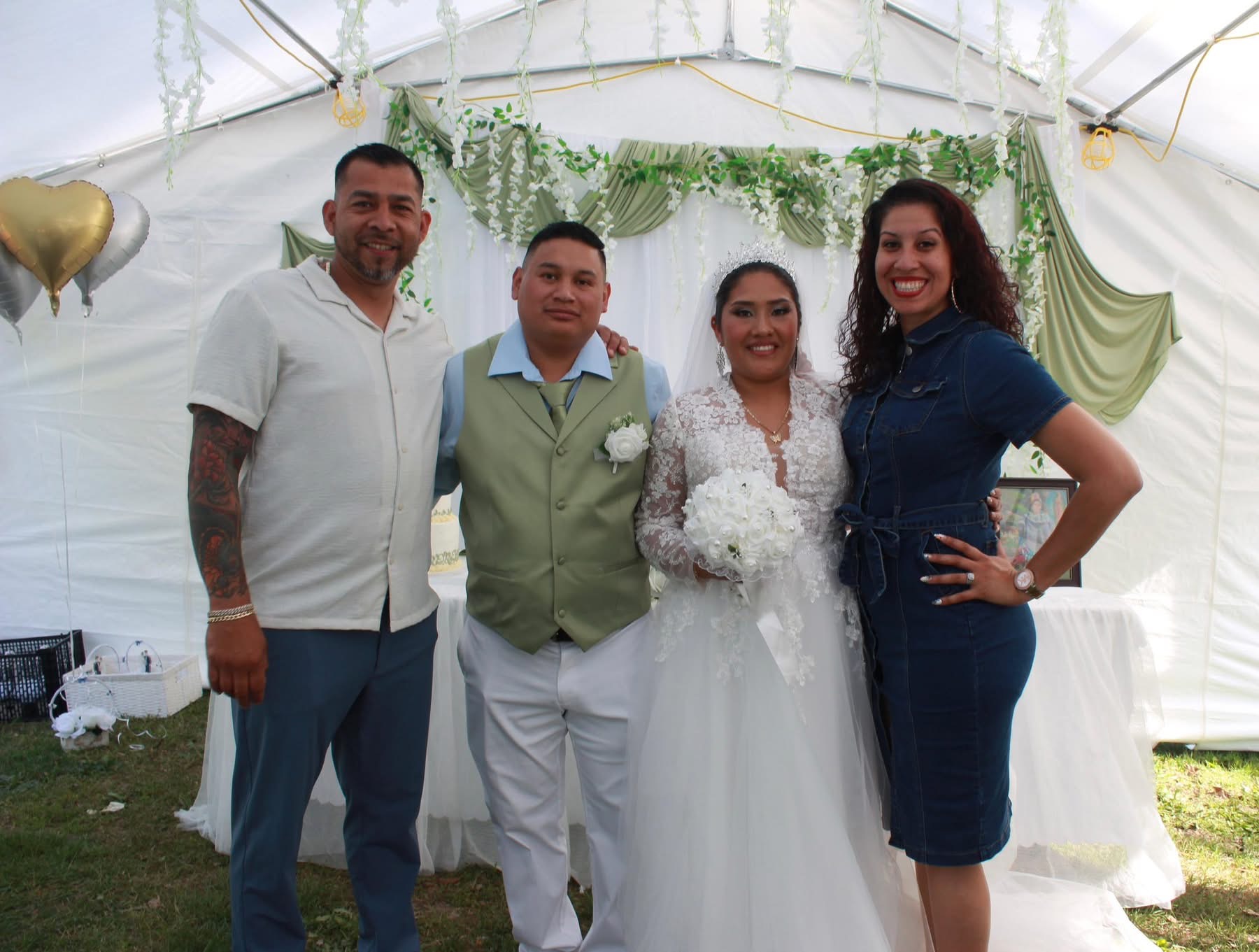 Four people standing together at a celebration, with a decorated white tent background, smiling and dressed formally.