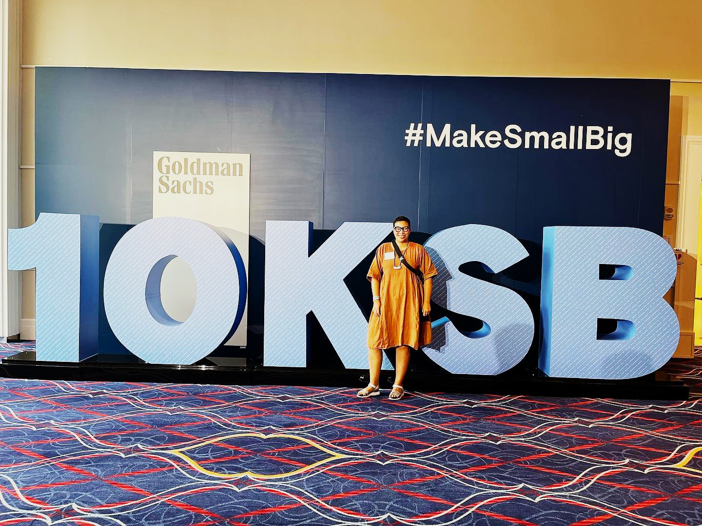 Person standing in front of large blue and white 10K SB letters at a conference, with a blue background and hashtag #MakeSmallBig.