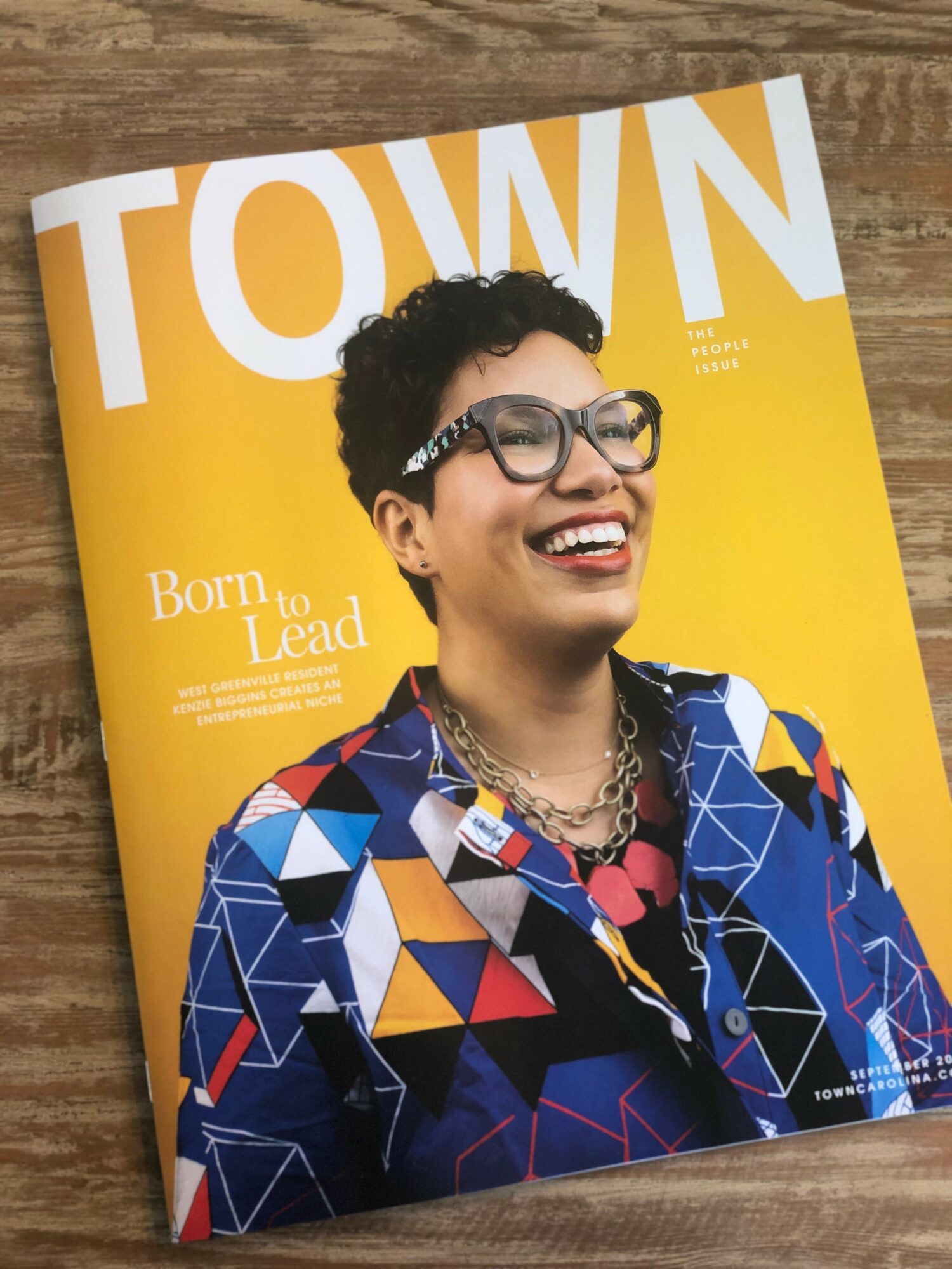 Woman with short curly hair, glasses, and colorful geometric-patterned jacket smiling on magazine cover.