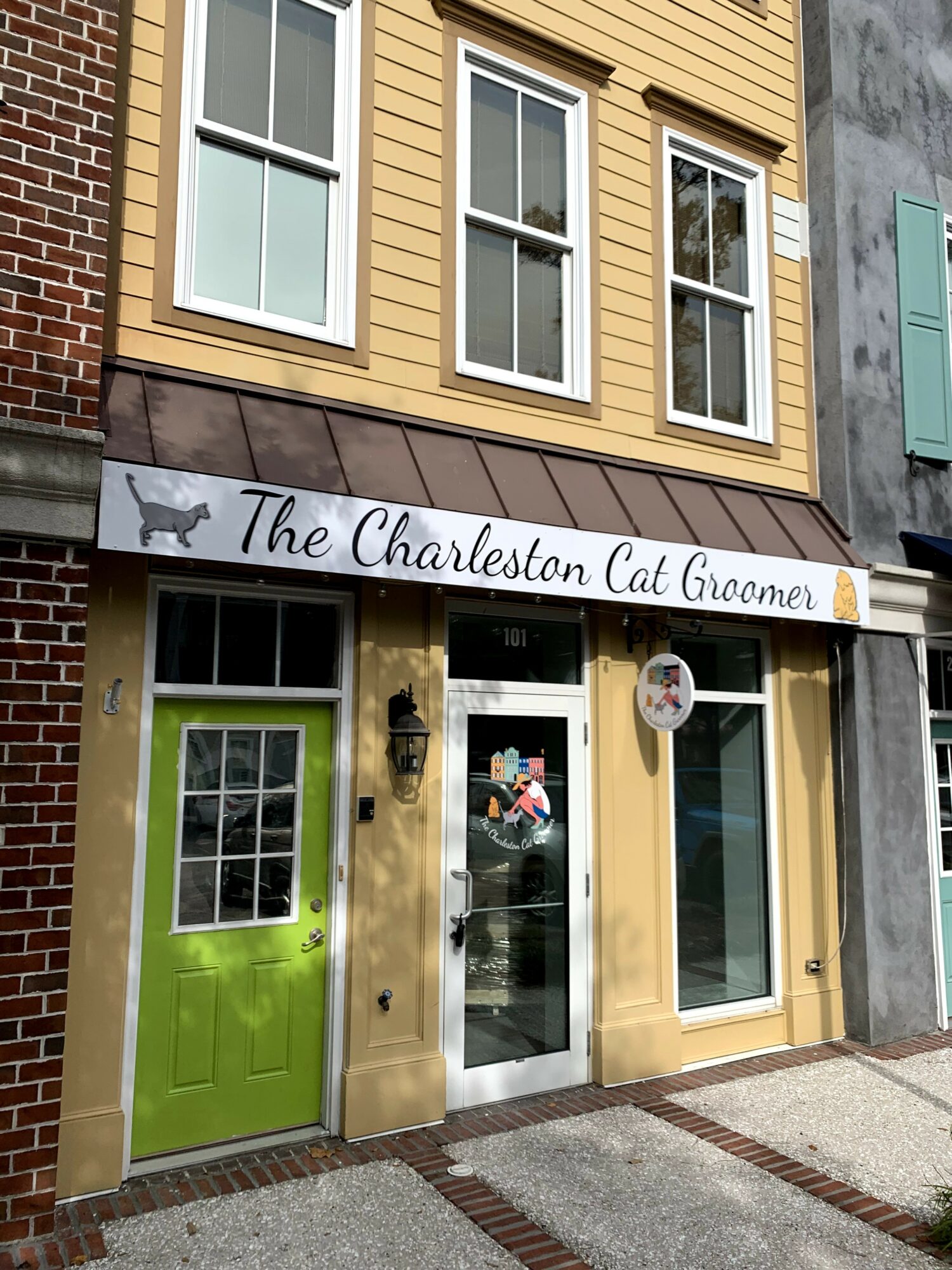 Storefront with a green door, large window, and sign reading 'The Charleston Cat Groomer' above the entrance.