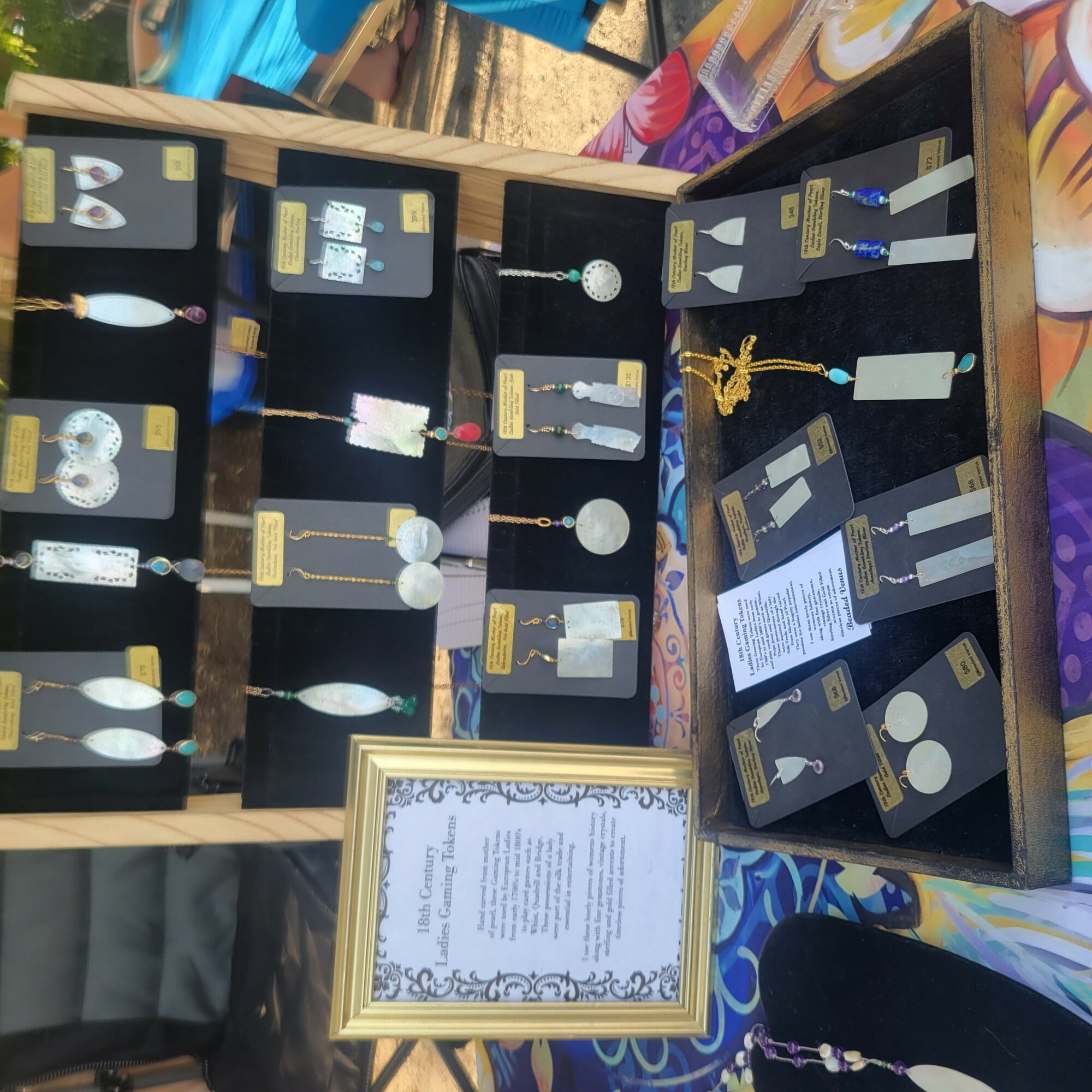 Display case with jewelry and medals, with a framed document in front, on a colorful tablecloth.