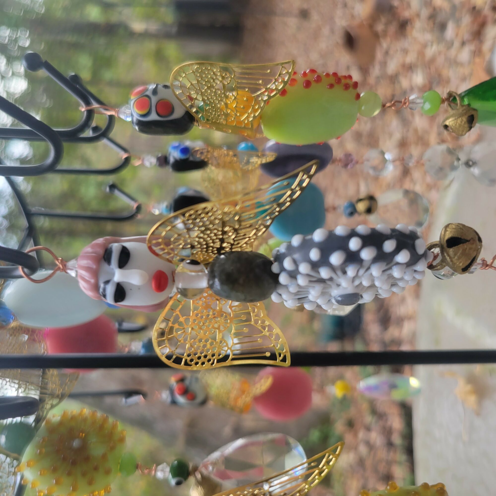 Colorful hanging decorations with insects and skulls, outdoors with trees and ground in background.