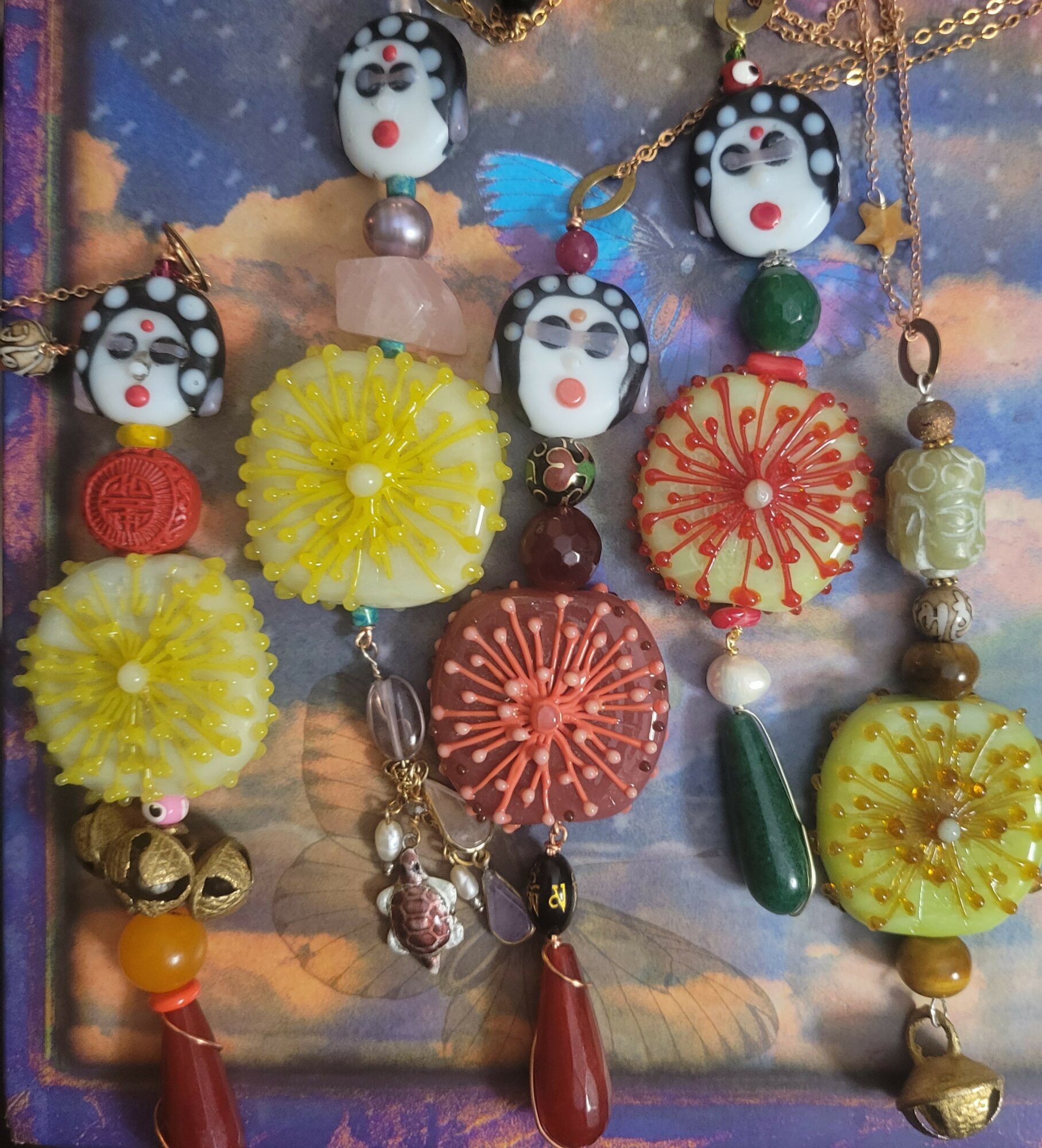 Collection of colorful jewelry pieces with various beads, charms, and decorative elements on a cloudy sky background.