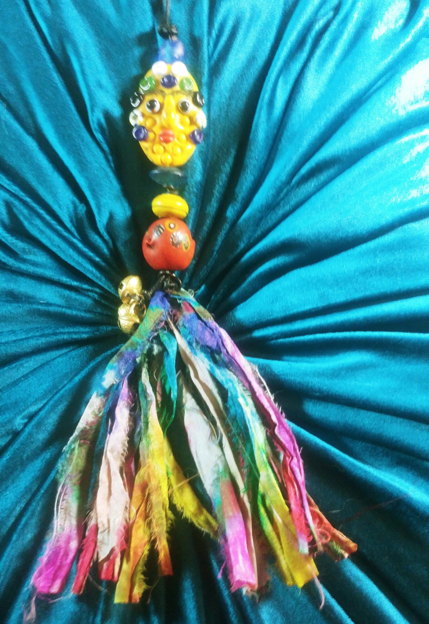 Colorful decorative item with beads and fabric hanging against a blue fabric background.