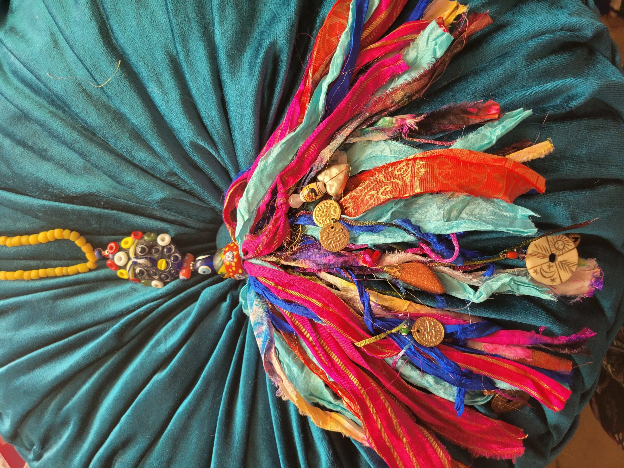 Colorful fabric with coins and beads, gathered in a circular pattern, on a teal background.