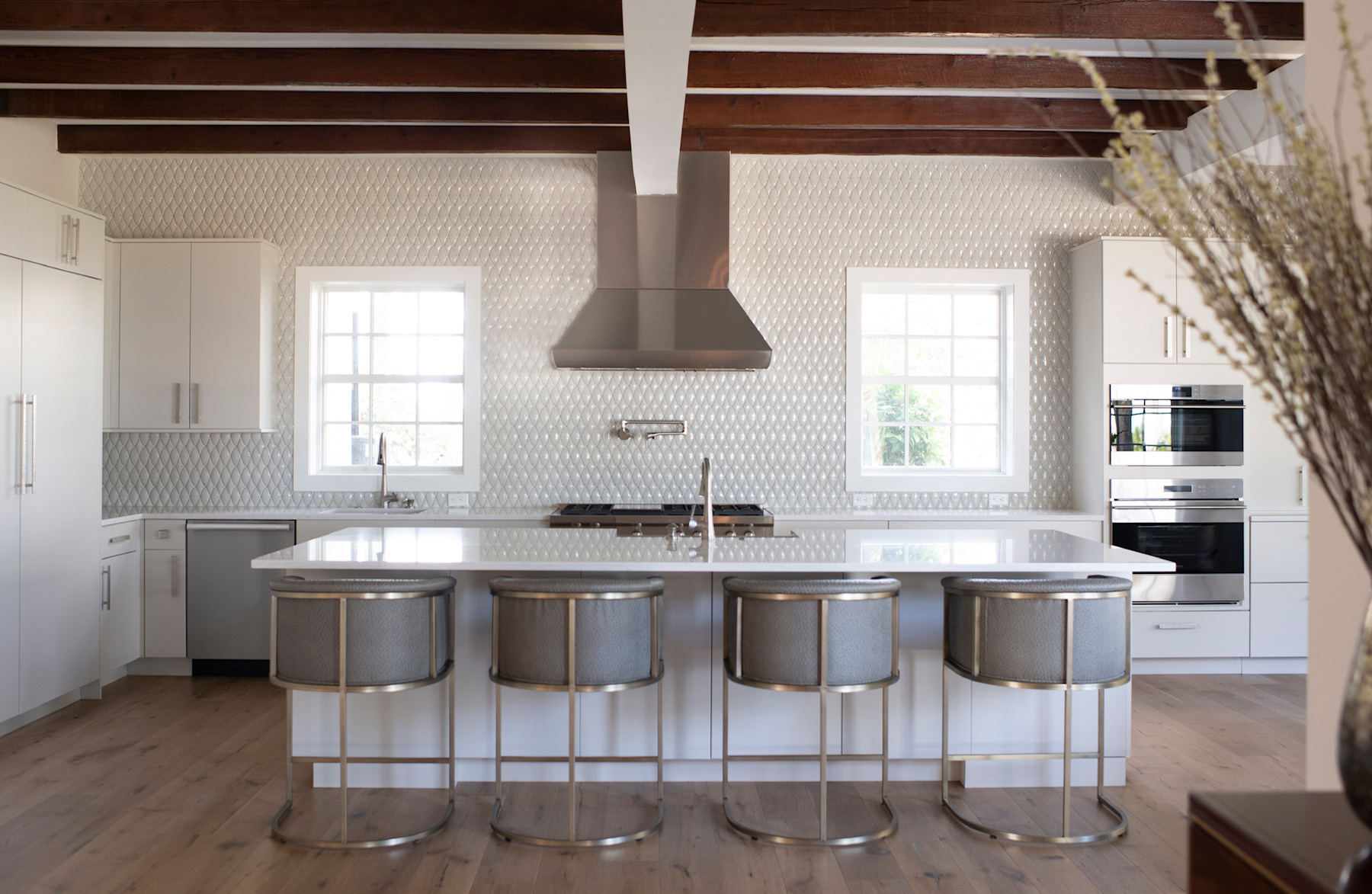 Modern kitchen with white cabinets, large island with five stools, stainless steel appliances, and two windows above the sink.
