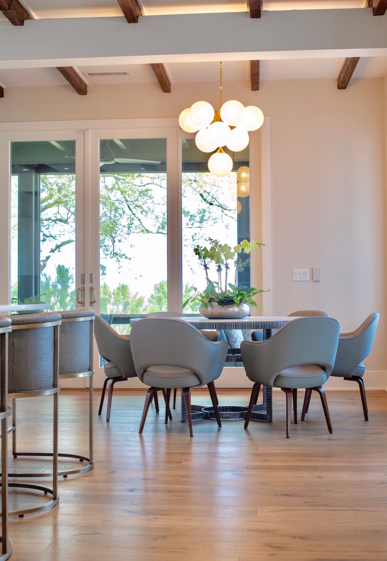 Dining area with a round table, six chairs, large window, and hanging light fixture, with wooden floor and ceiling beams.