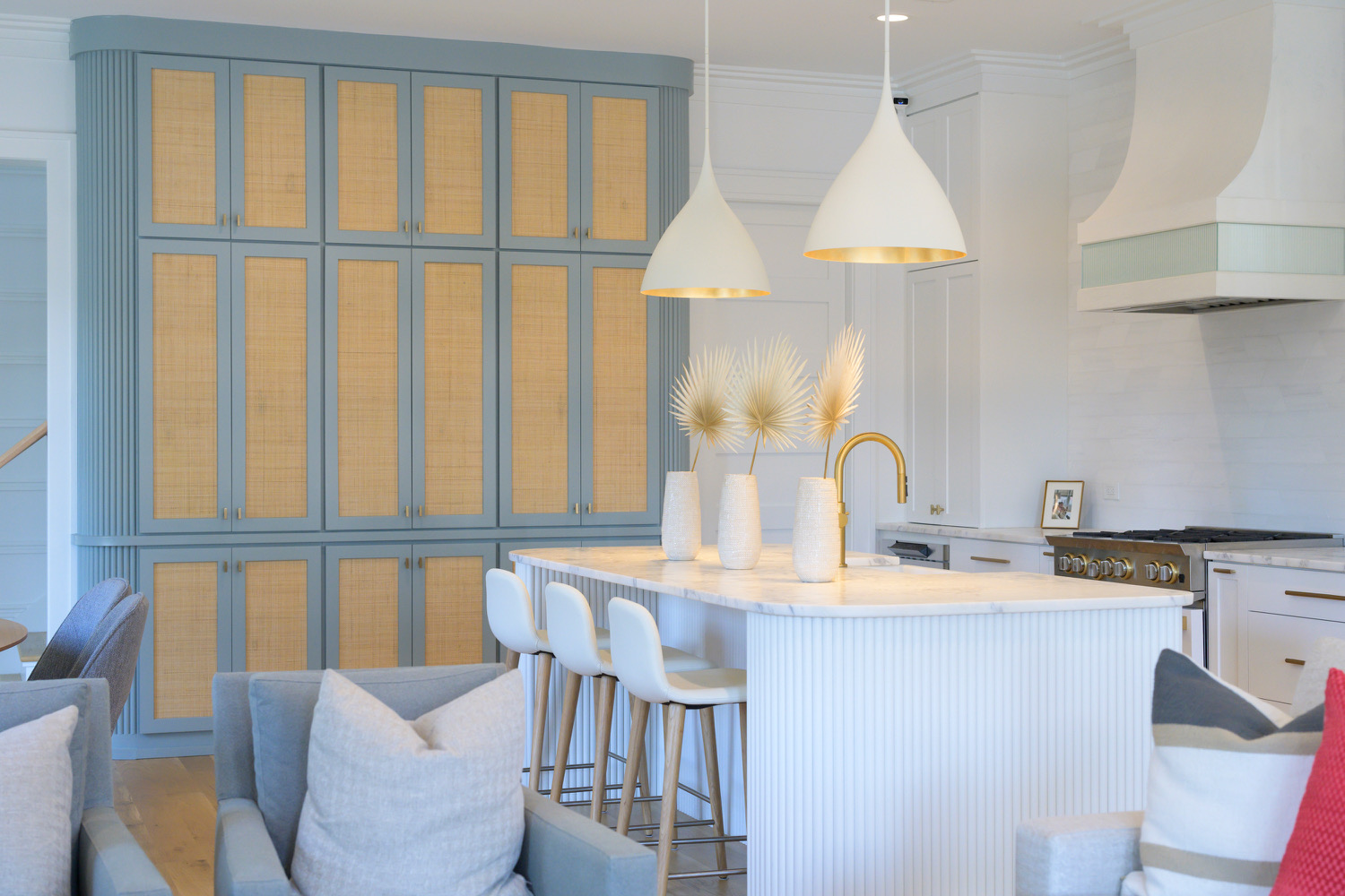 Modern kitchen with white cabinets, a blue and wood-paneled wall, and a white island with bar stools, pendant lights, and decorative vases.